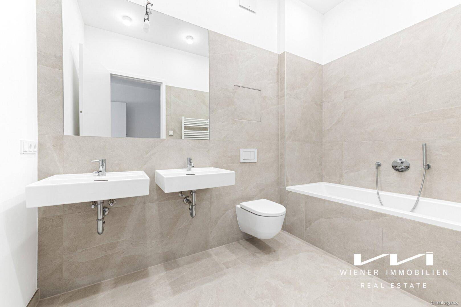 Modernes Badezimmer mit zwei Waschbecken, Badewanne und eleganten großformatigen Fliesen an Wänden und Boden.