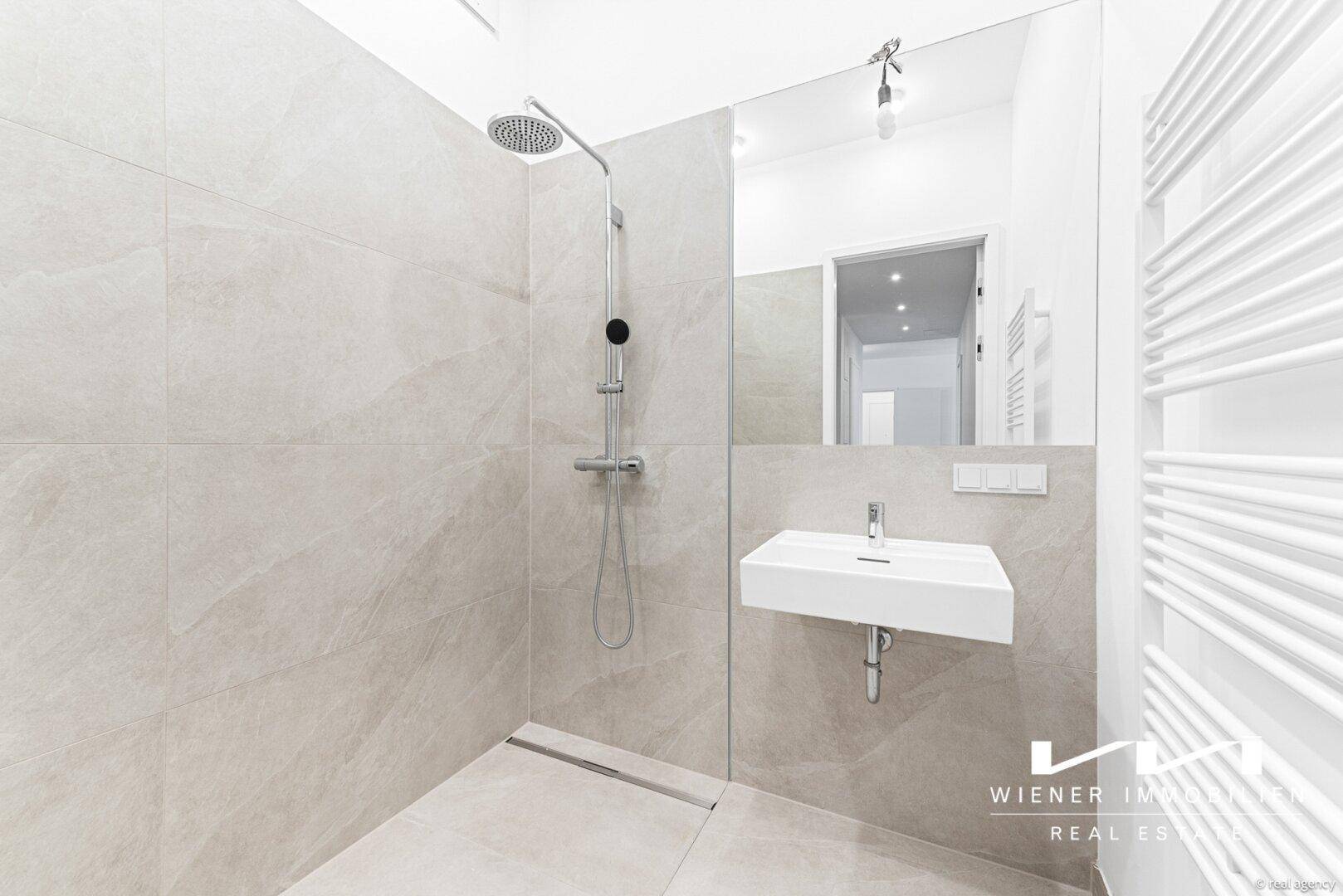 Modernes Badezimmer mit ebenerdiger Dusche, elegantem Waschbecken und großem Spiegel.