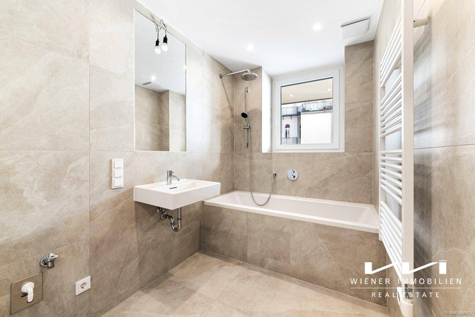Modernes Badezimmer mit beigefarbenen Fliesen, Badewanne, Dusche und Fenster für Tageslicht.