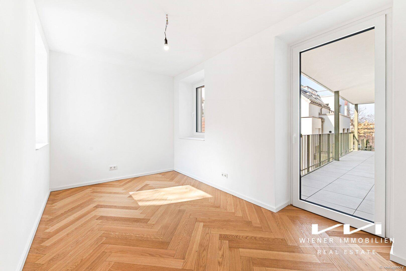 Schlafzimmer mit Fischgrätparkett, weißen Wänden und direktem Zugang zum Balkon.
