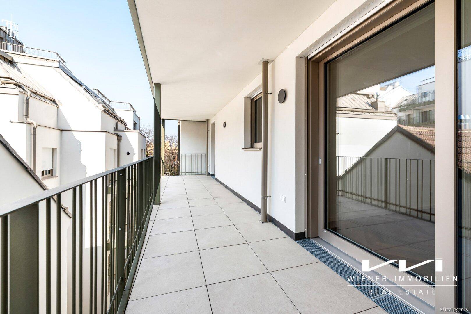 Langer, gefliester Balkon mit moderner Brüstung und Blick auf umliegende Gebäude.
