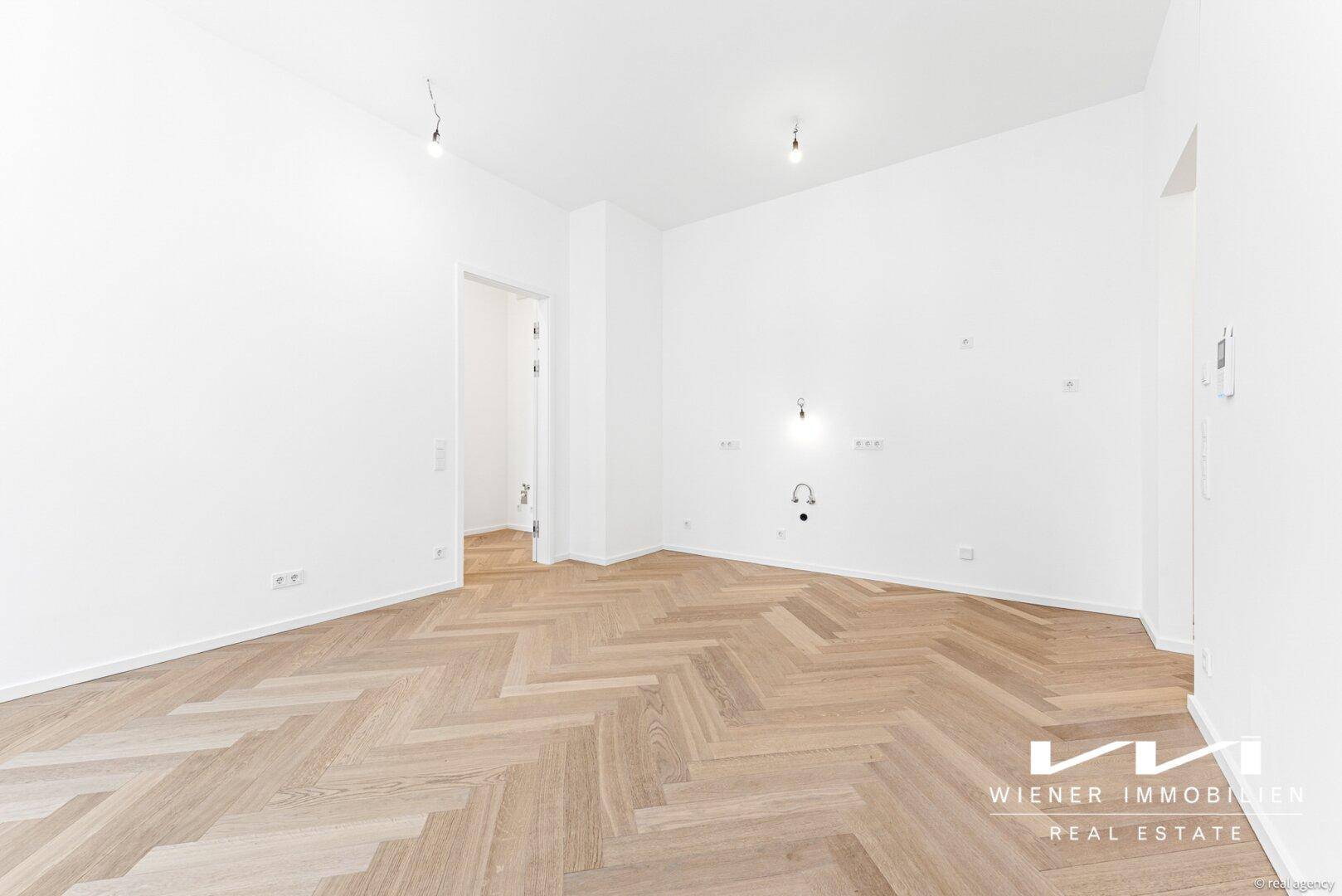 Geräumiges, helles Zimmer mit elegantem Fischgrätparkett und weißen Wänden, bereit zur Einrichtung.