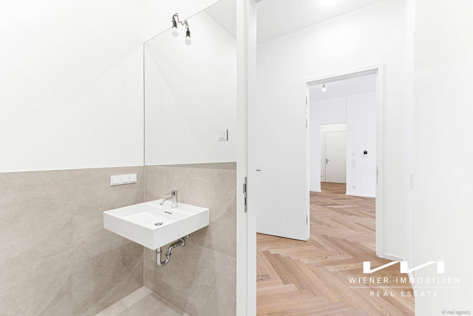 Modernes Badezimmer mit schwebendem Waschbecken, großem Spiegel und hellen Fliesen an der Wand.