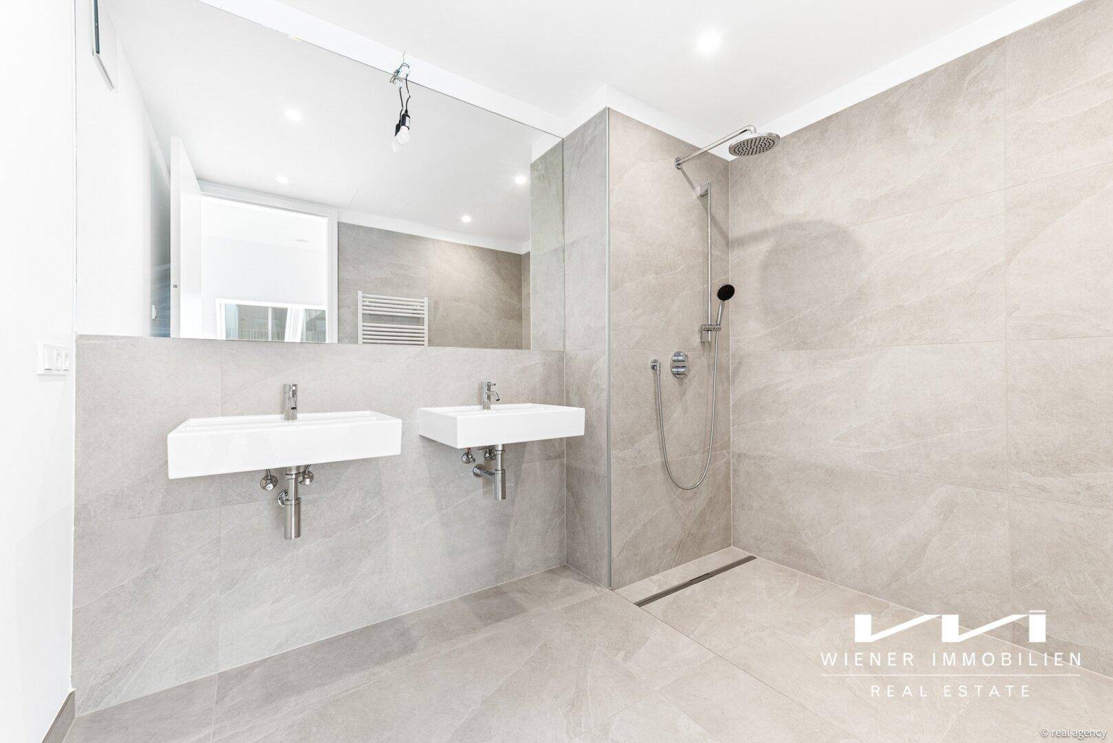Modernes Badezimmer mit doppelten Waschbecken, großer Dusche und hellen Fliesen.