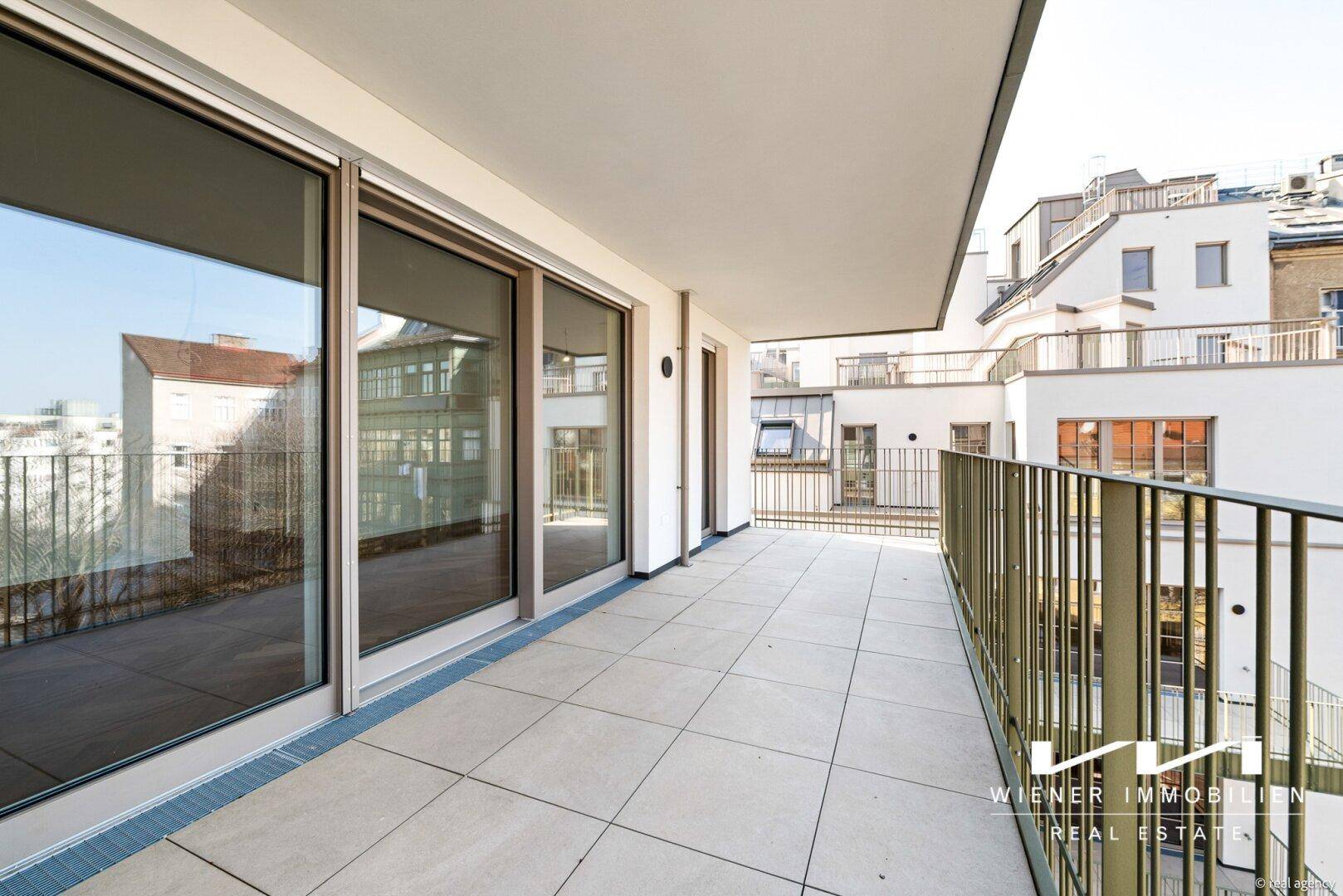 Geräumiger Balkon mit Fliesenboden und Metallgeländer, bietet einen Blick auf die umliegenden Gebäude.