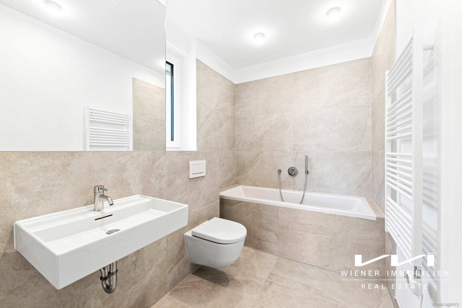 Modernes Badezimmer mit Badewanne, Wand-WC, Einzelwaschbecken und hellen, großformatigen Fliesen.