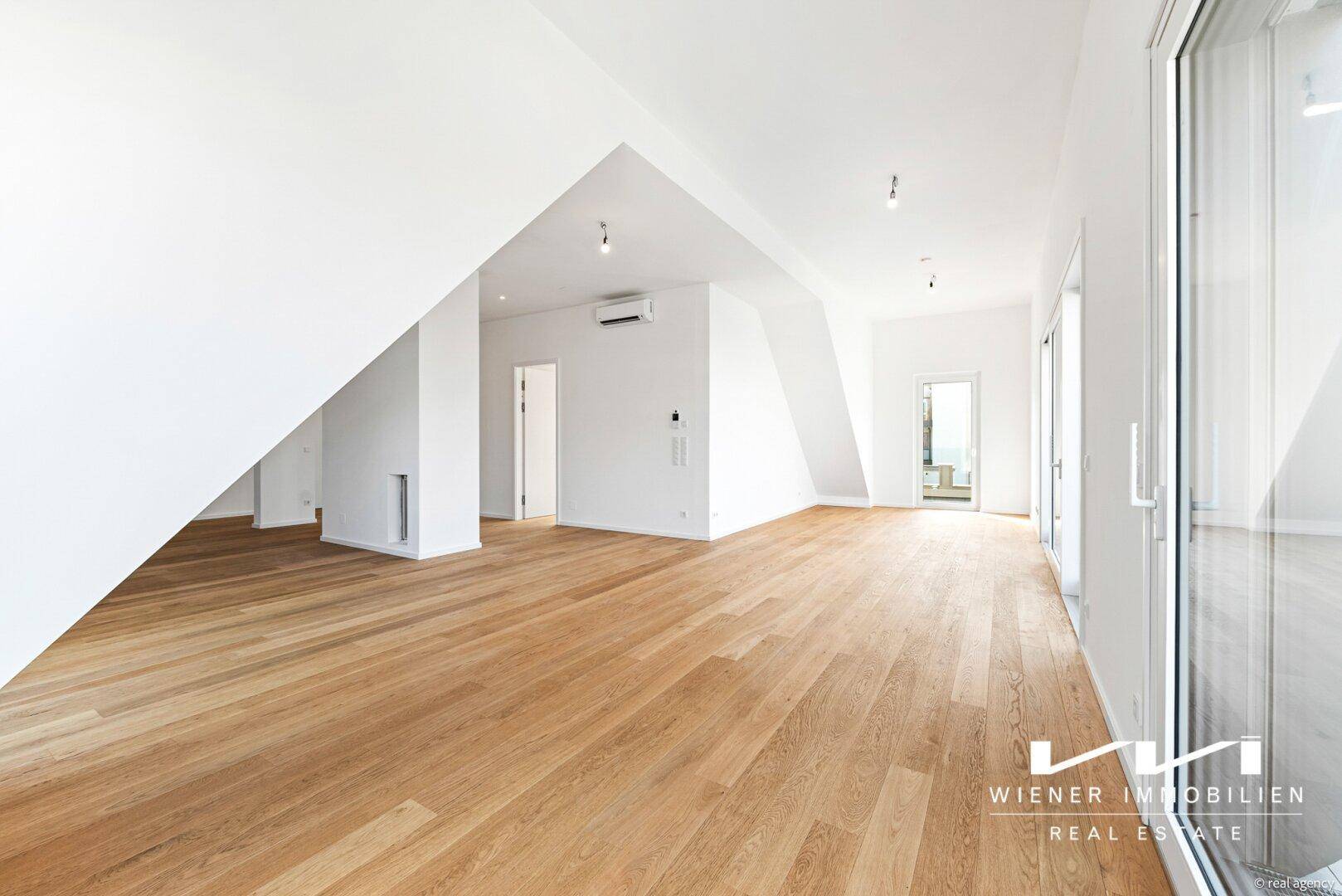 Lichtdurchfluteter Wohnbereich im Dachgeschoss mit elegantem Holzboden, hohen Wänden und großen Fensterfronten.