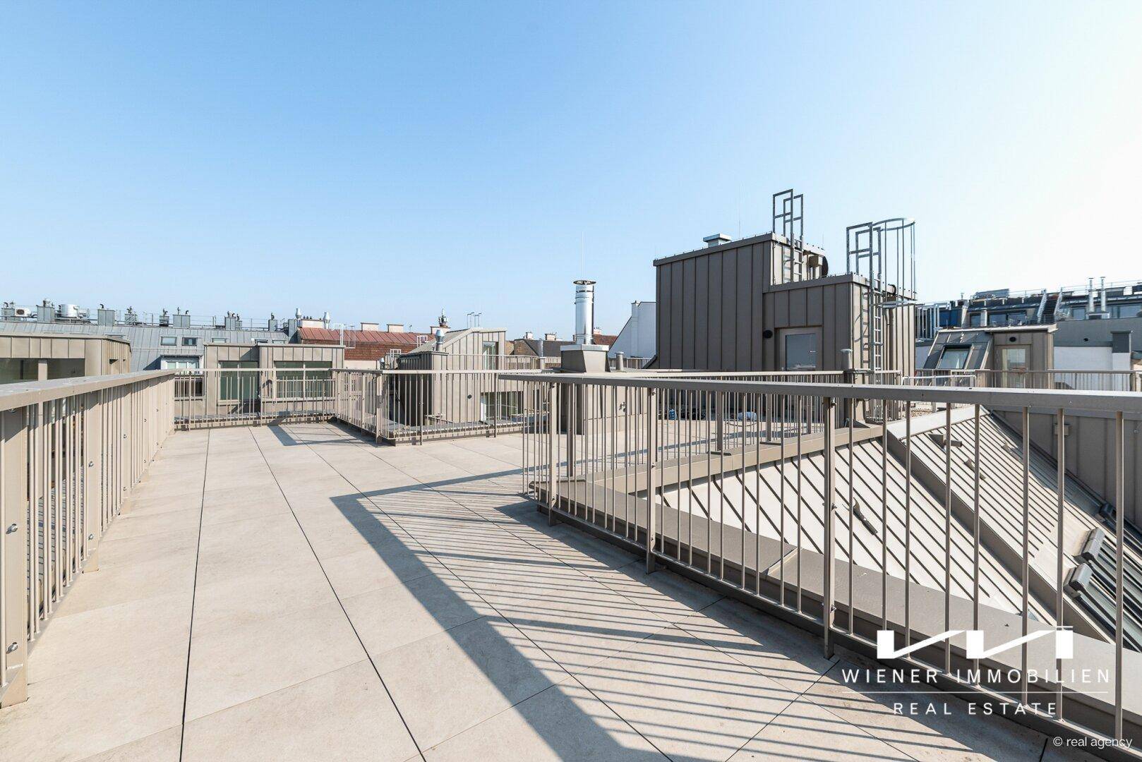 Weitläufige Dachterrasse mit Metallgeländer und Panoramablick über die umliegenden Dächer der Stadt.