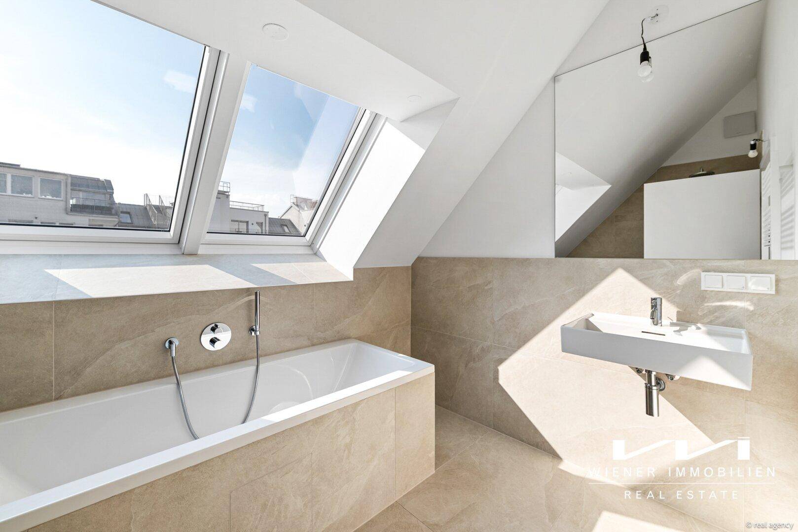 Modernes Badezimmer im Dachgeschoss mit Badewanne, Waschtisch und großen Dachfenstern für viel Licht.