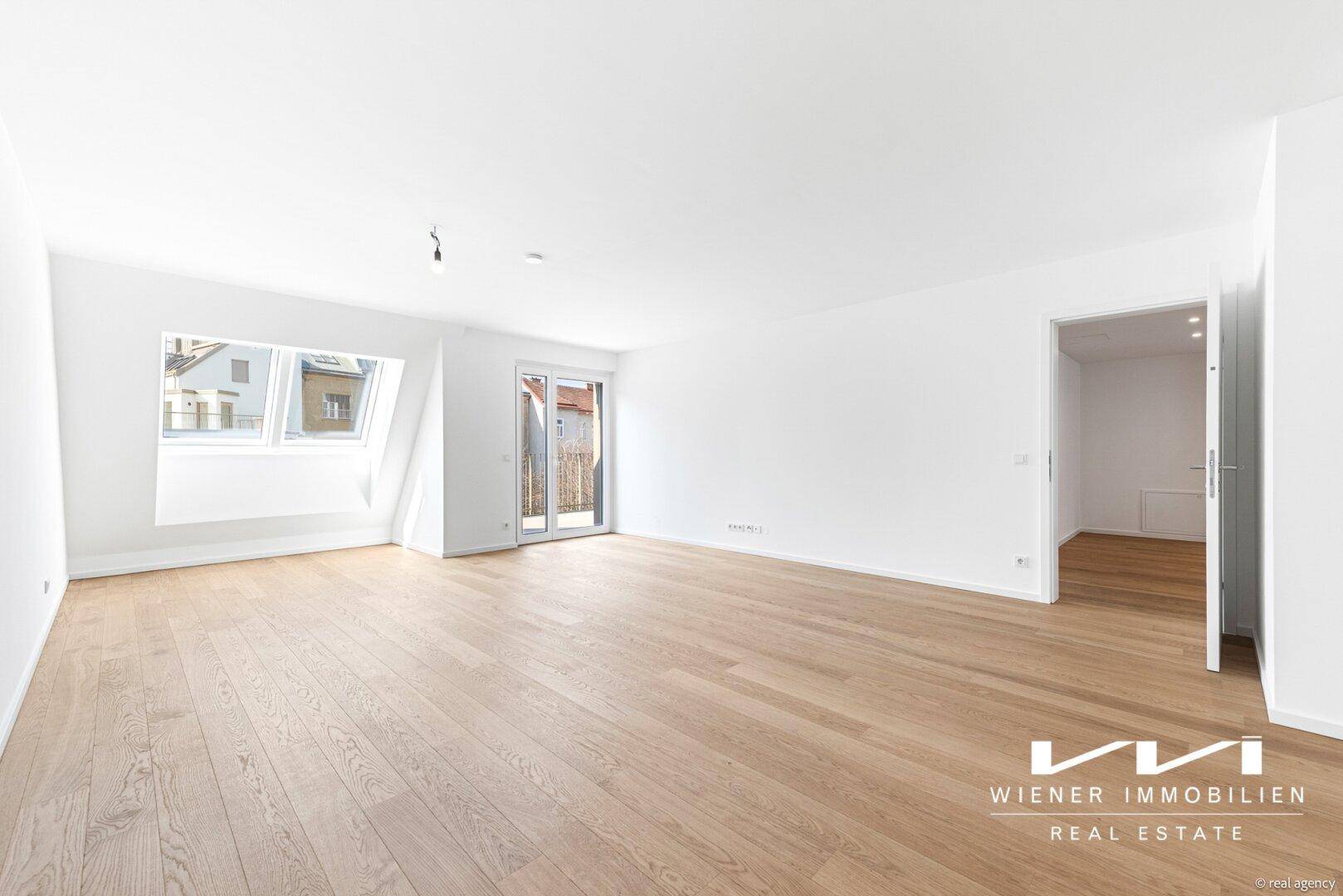 Heller, leerer Raum mit Holzboden, Dachschrägenfenstern und Zugang zu einem Außenbereich.