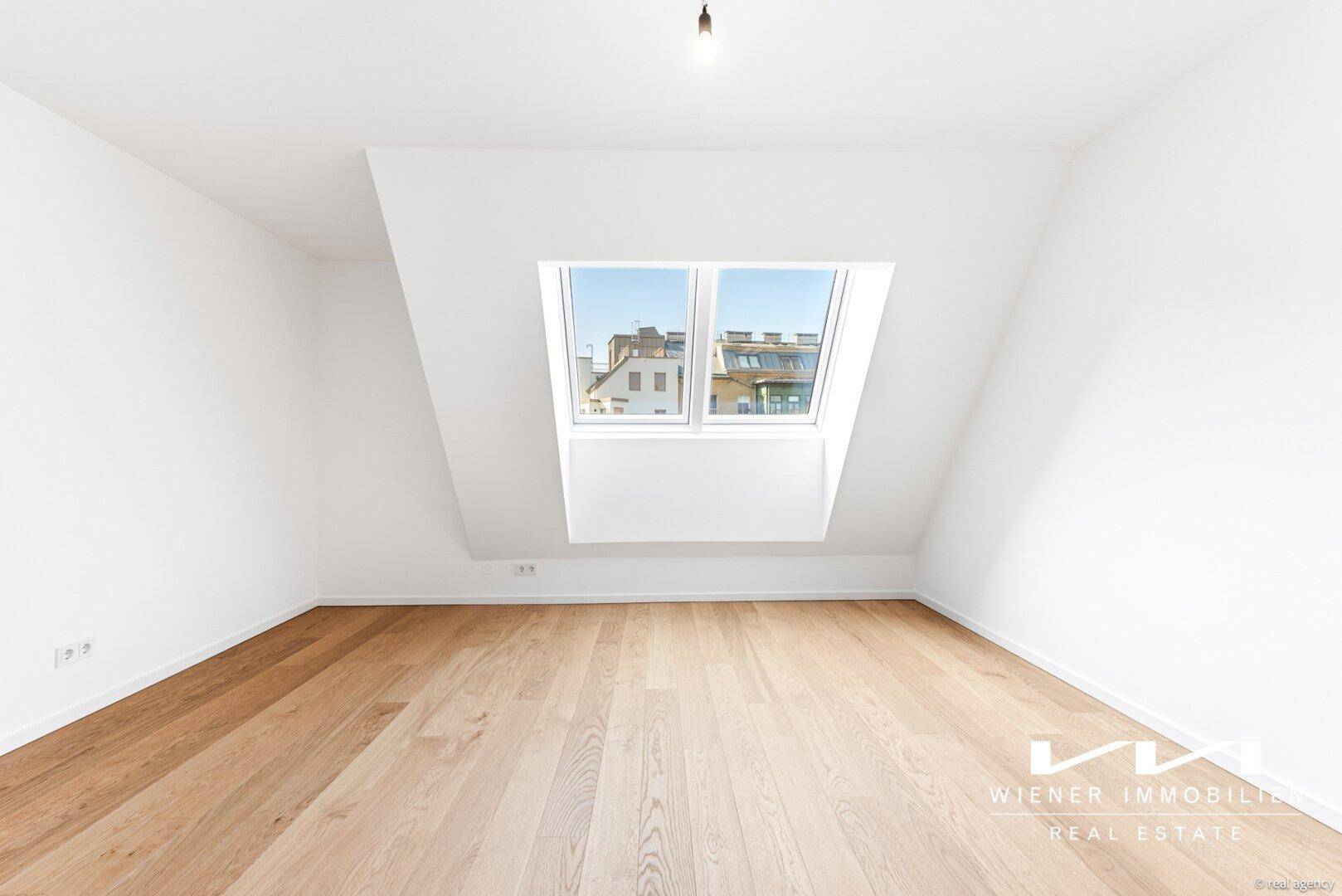 Ruhiges Zimmer mit Holzboden und großem Dachfenster, ideal als Schlaf- oder Arbeitszimmer.