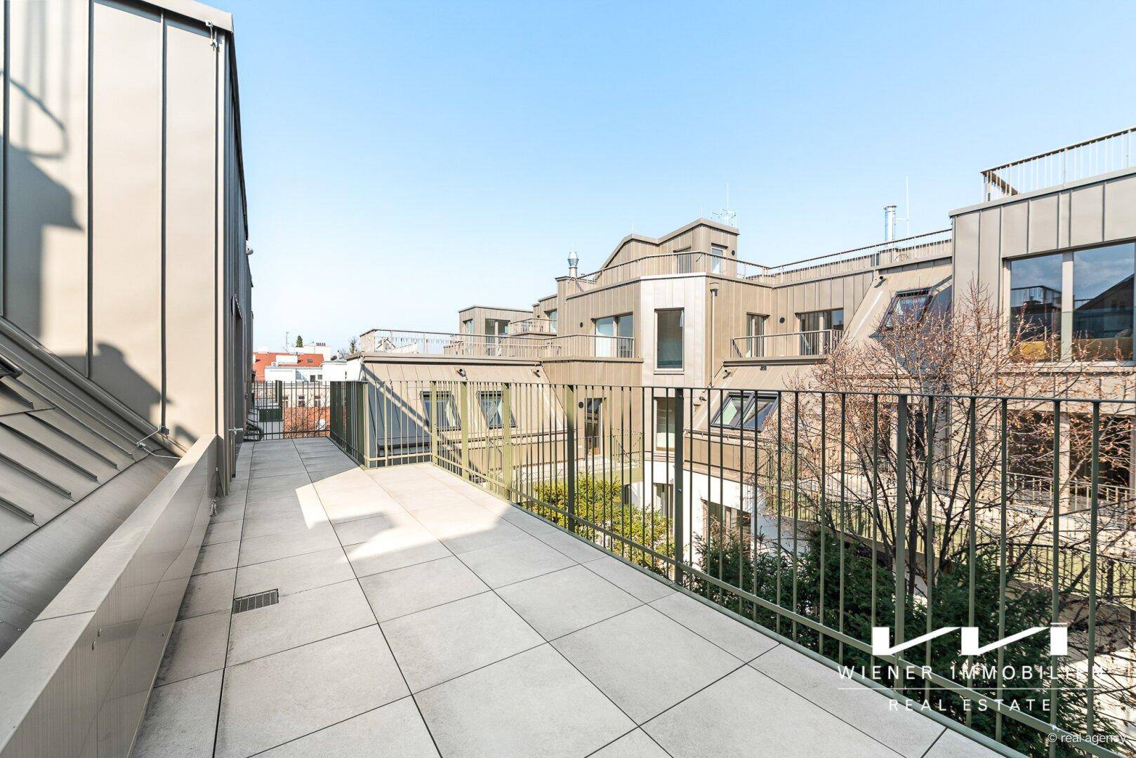 Langer Balkon mit Fliesenboden und Blick auf den begrünten Innenhof.