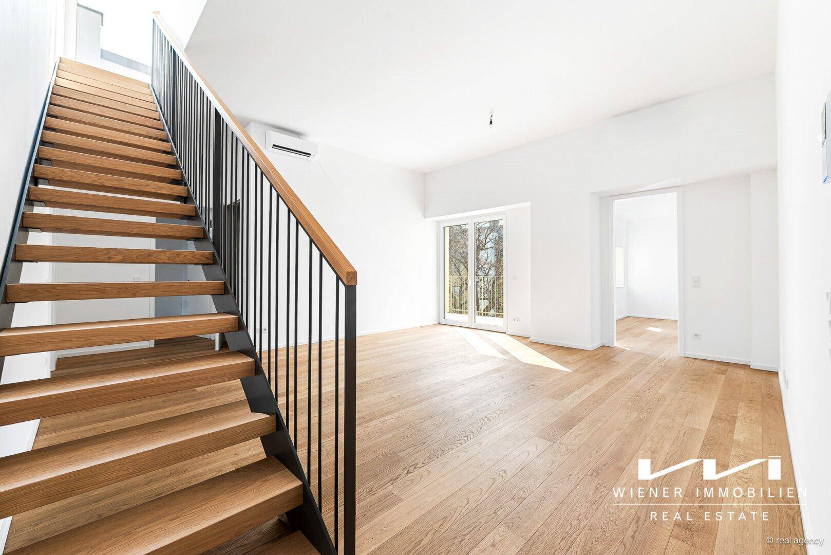 Heller Wohnbereich mit eleganter Holztreppe und Zugang zu einem französischen Balkon.