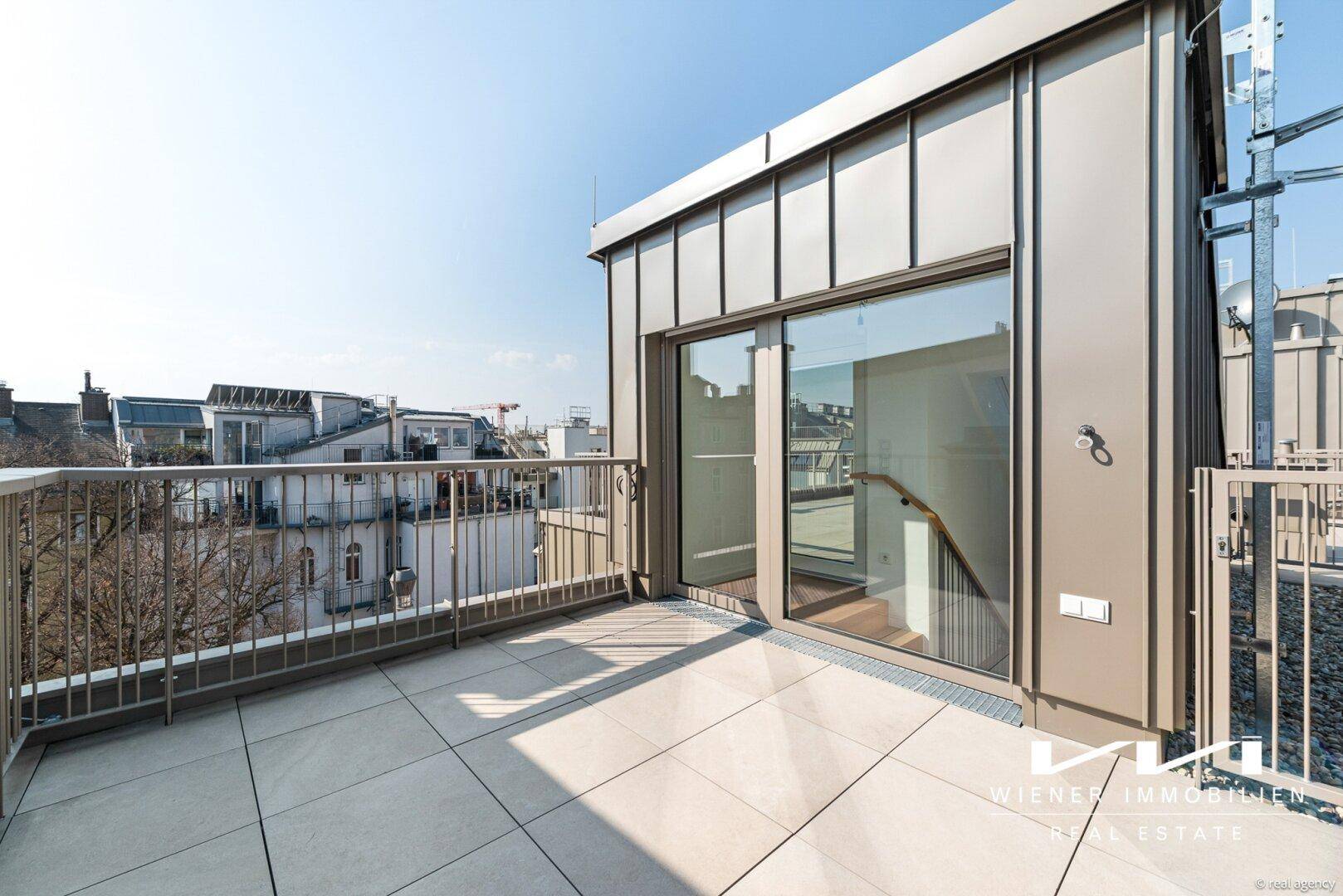 Heller Balkon mit Fliesenboden und Zugang zum Innenbereich durch eine große Glastür.