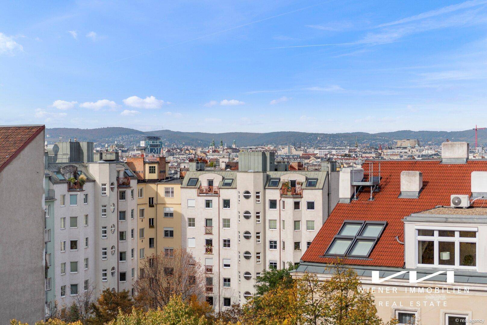 Weitläufiger Stadtblick über Wohngebäude und Dächer mit grünen Hügeln im Hintergrund.