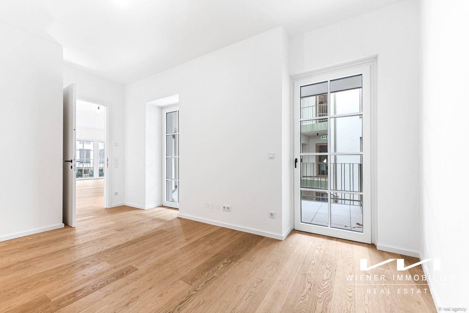 Geräumiger Raum mit Parkettboden und Zugang zu einem französischen Balkon.