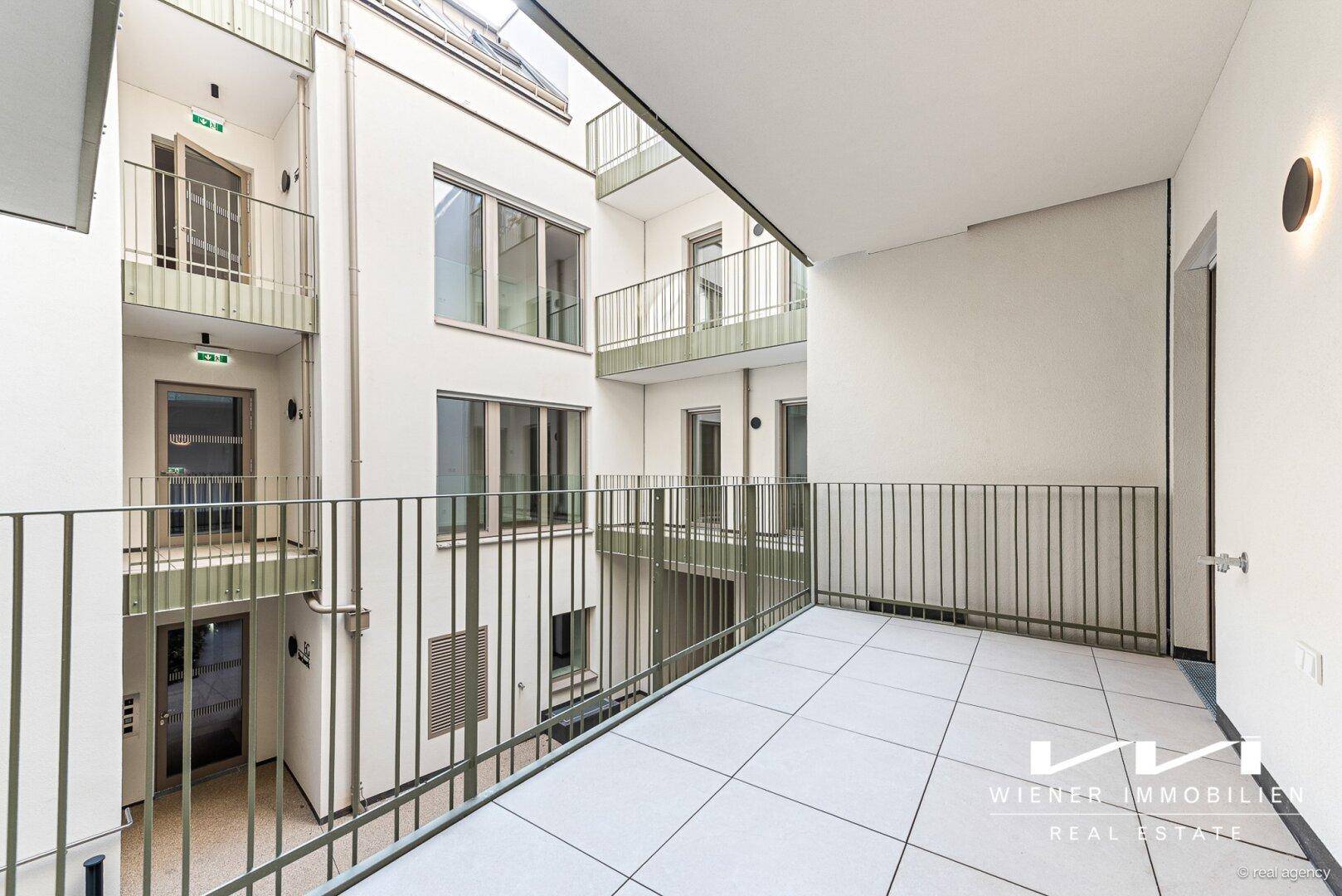 Balkon mit Blick auf den begrünten Innenhof und die umliegenden Gebäude.