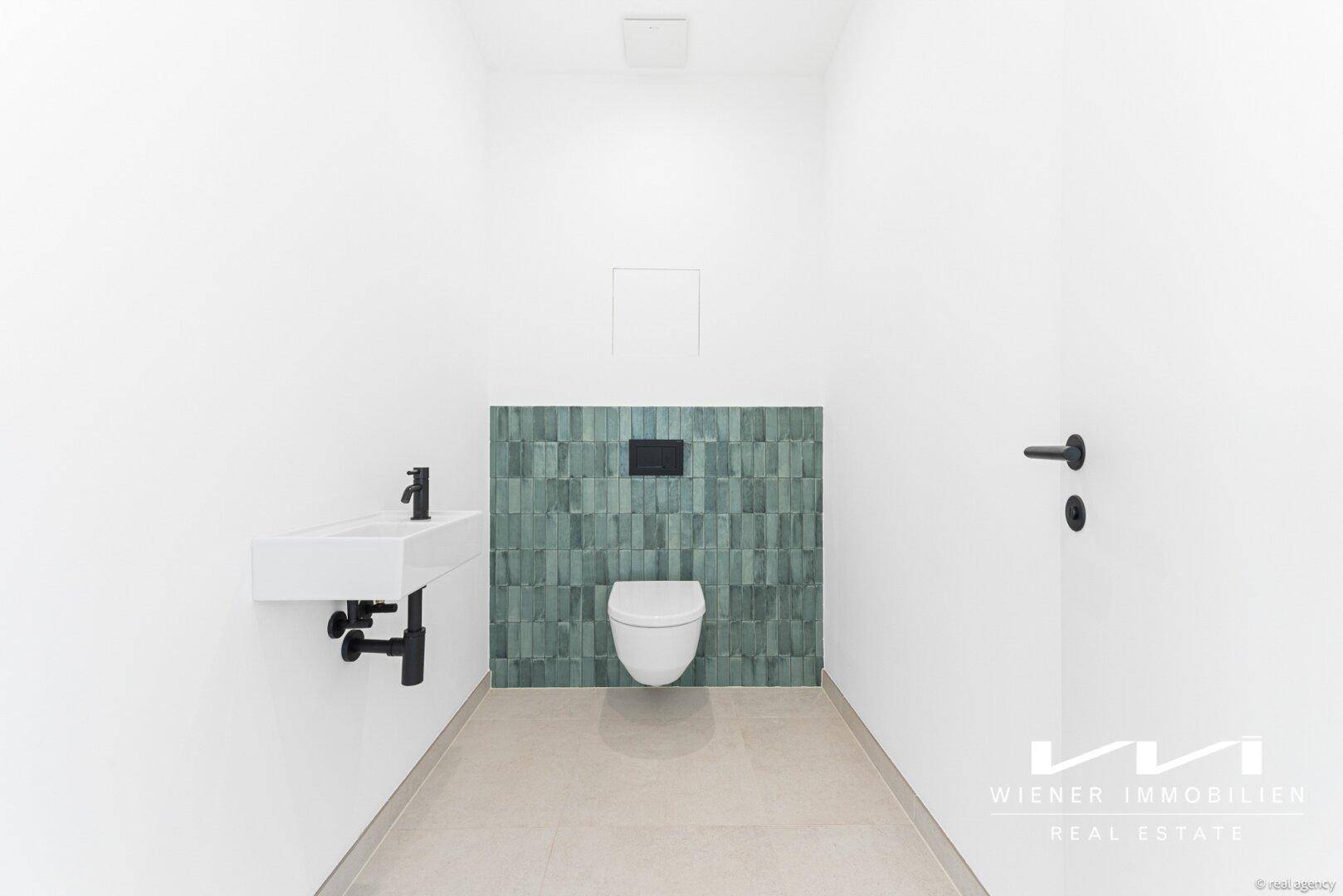 Gäste-WC mit wandhängender Toilette, modernem Waschbecken und grünen Akzentfliesen.