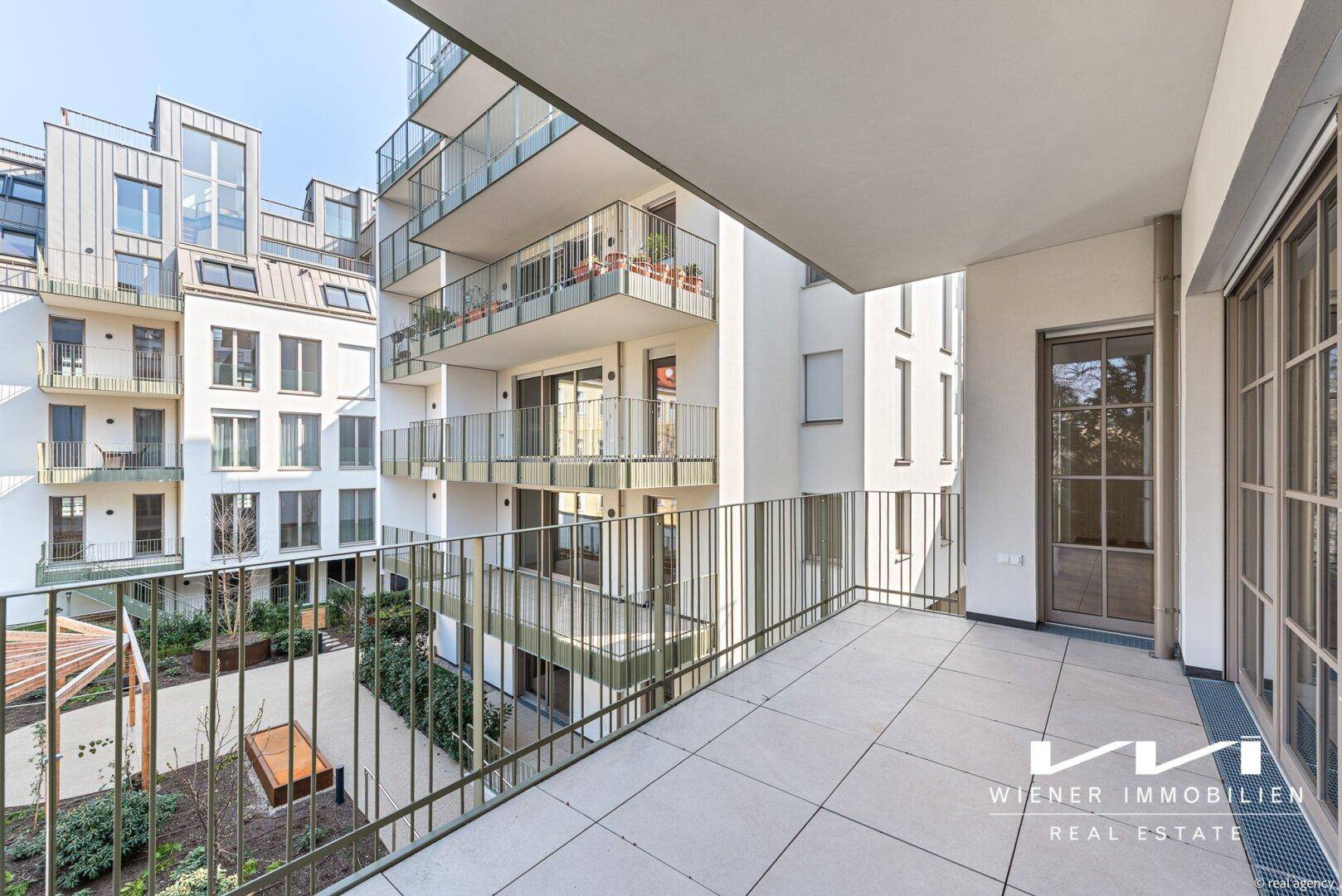 Geräumiger Balkon mit Fliesenboden und Blick auf den begrünten Innenhof des Gebäudes.