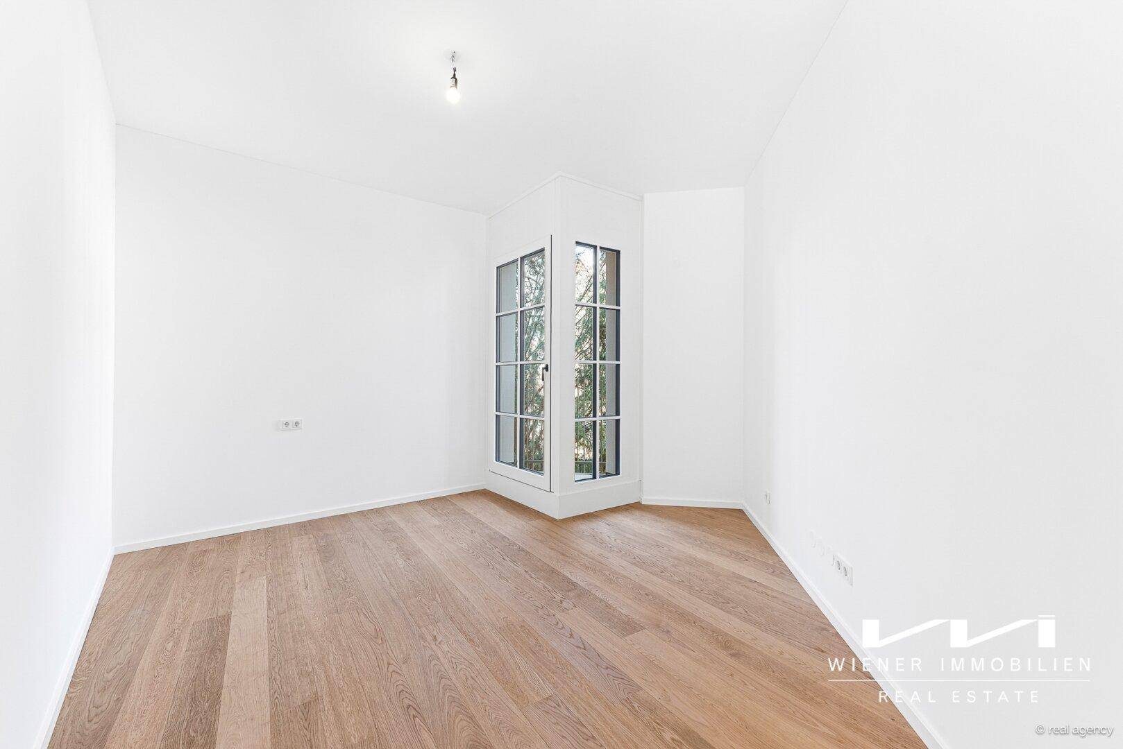 Helles Zimmer mit Holzparkettboden und einem charmanten Eckfenster.
