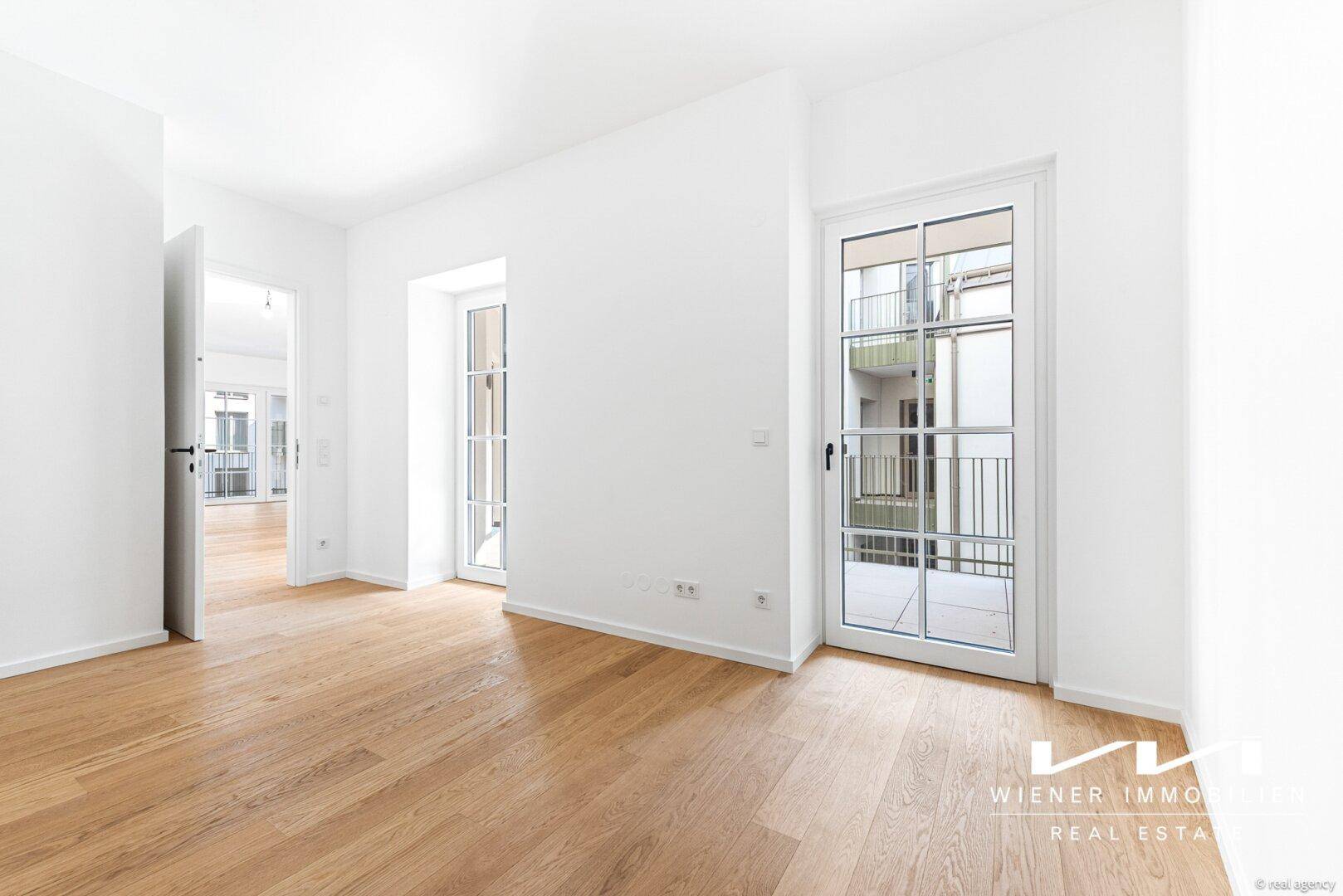 Heller Raum mit Holzparkettboden und Zugang zu einem Balkon mit Blick auf den Innenhof.