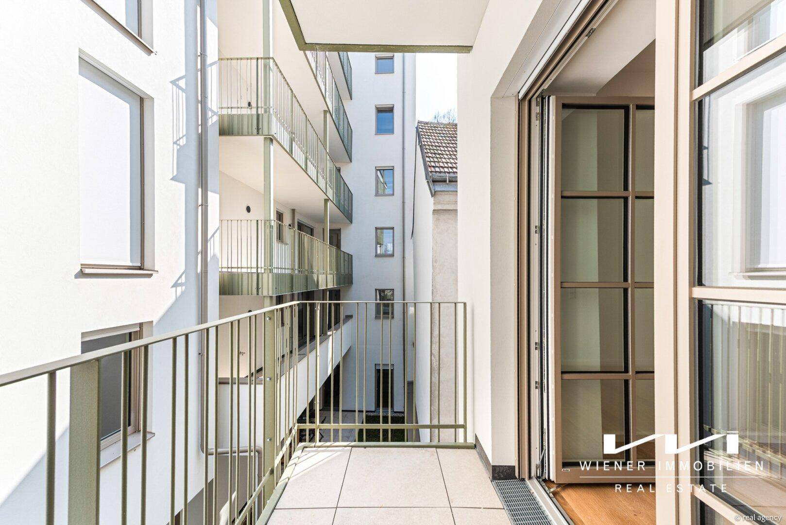 Kleiner Balkon mit Fliesenboden und Blick auf die umliegenden Gebäudefassaden.