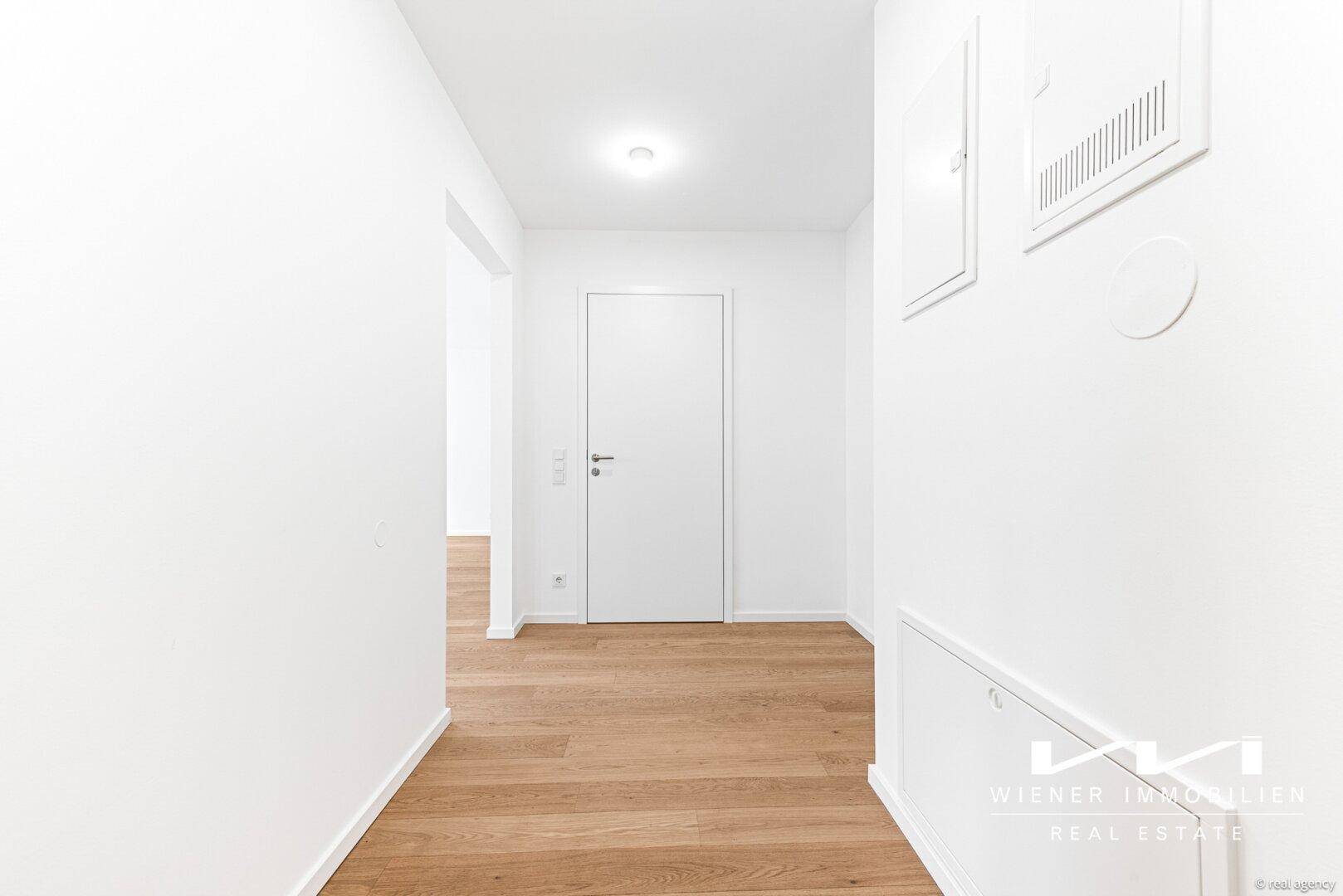 Heller Flur mit Holzboden und weißen Wänden, der verschiedene Räume verbindet.