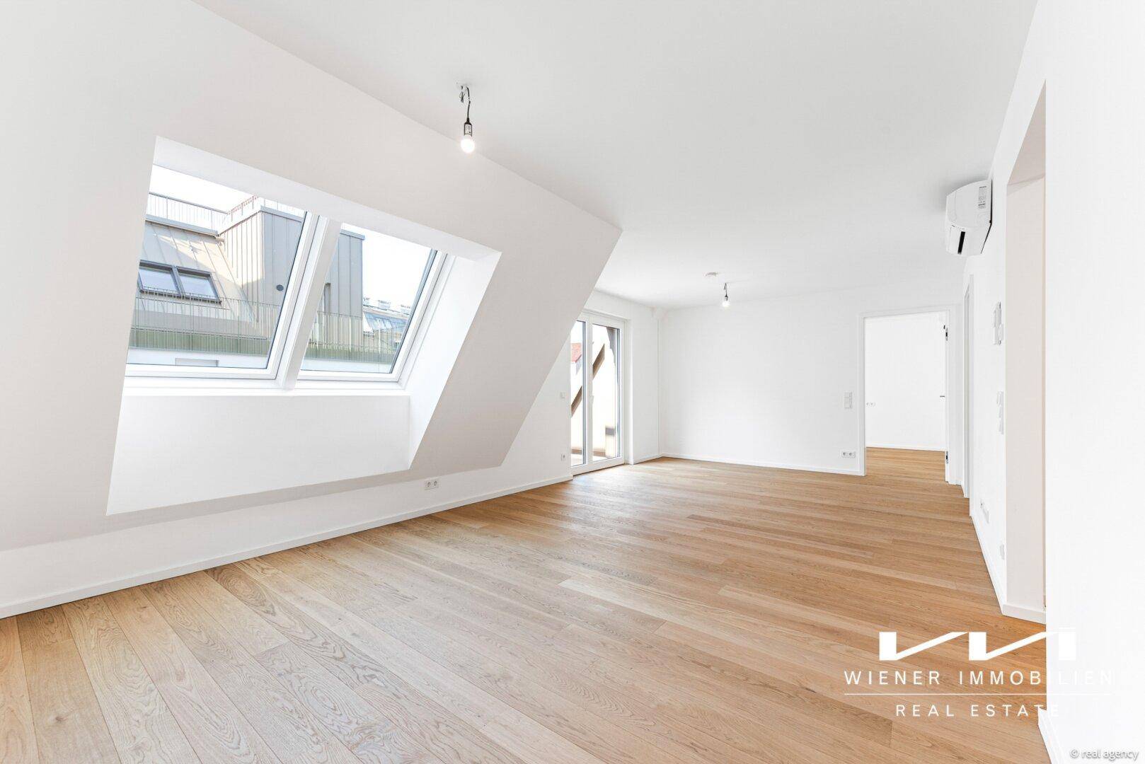 Lichtdurchfluteter Wohnraum mit Holzboden, schrägen Wänden, Dachfenstern und Balkontür.