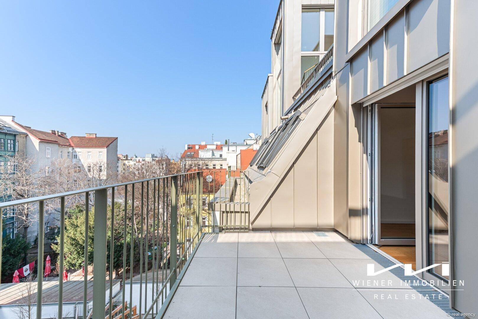 Geräumiger Balkon mit Fliesenboden und Blick über die Stadt und umliegende Gebäude.