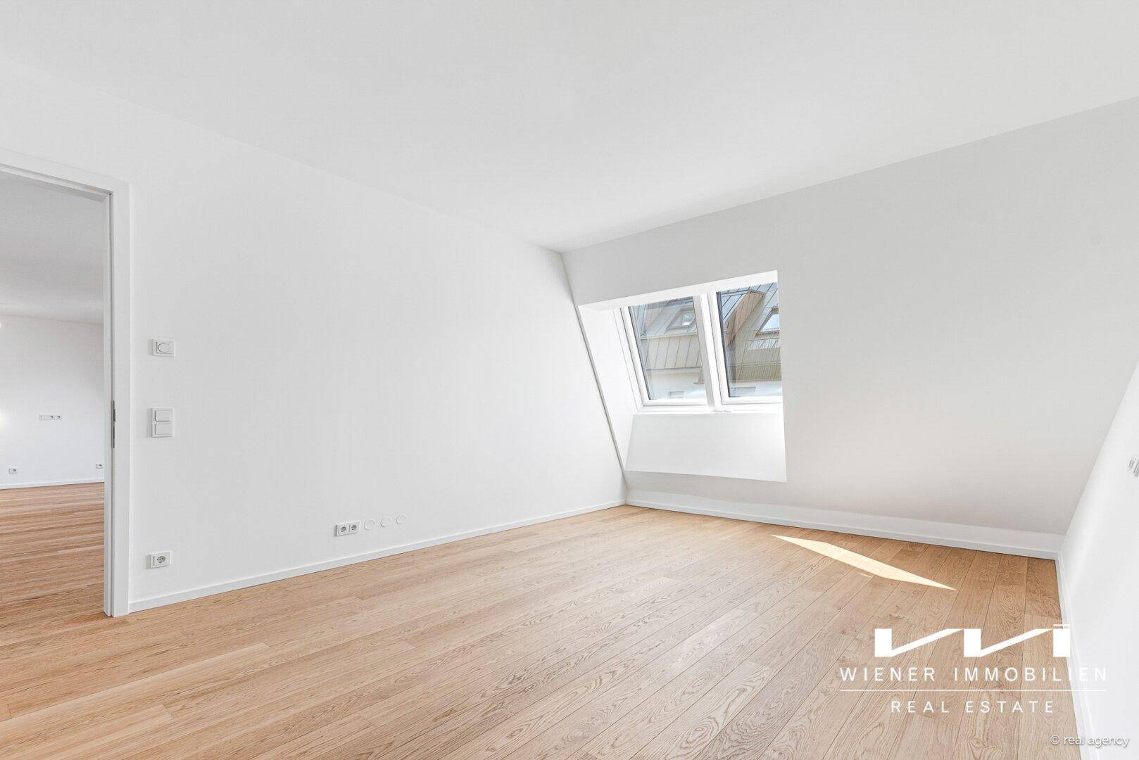 Helles Schlafzimmer mit Eichenparkett, Dachschräge und einem großen Dachfenster.