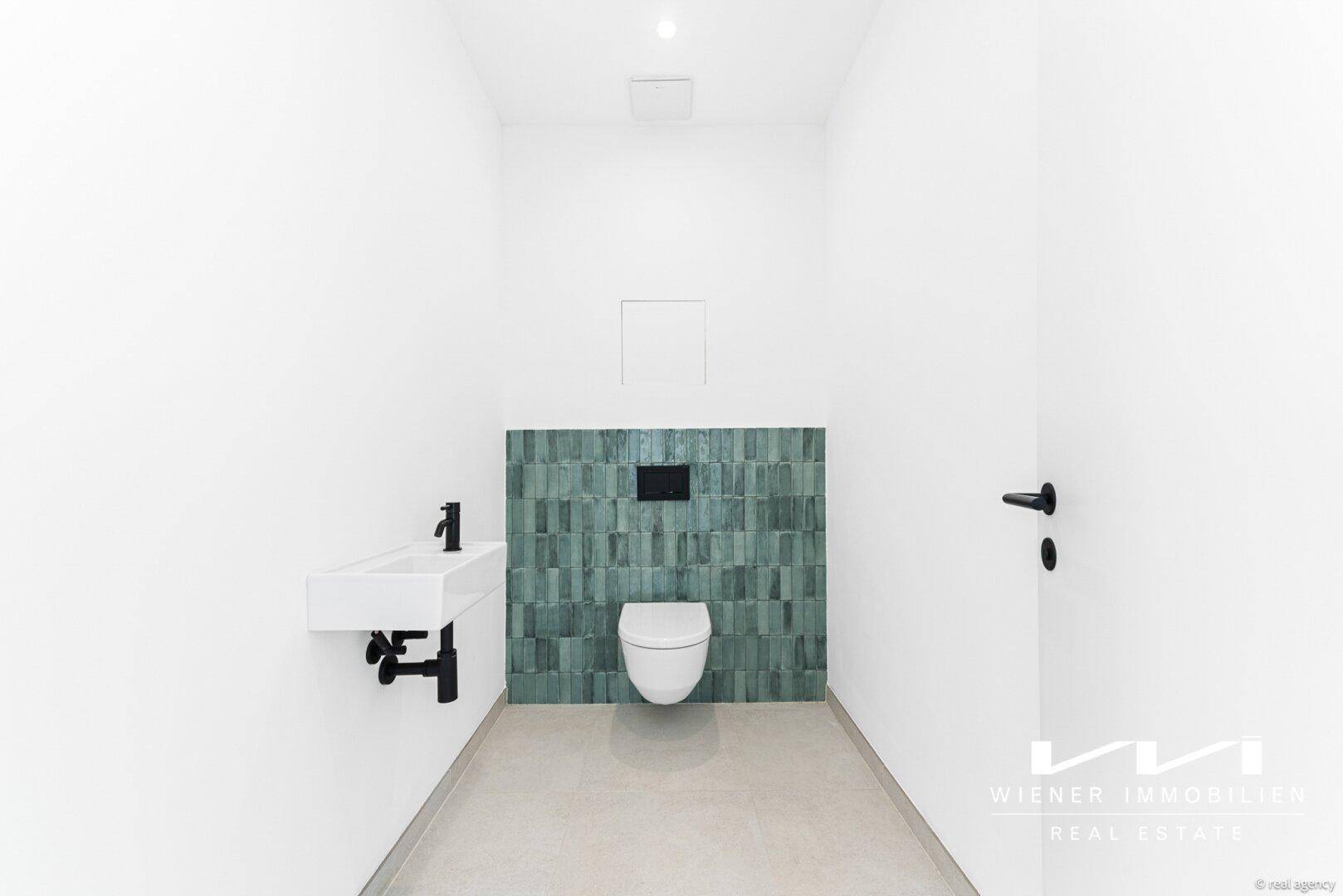 Modernes Gäste-WC mit Wand-WC, kleinem Waschbecken und türkisfarbenen Akzentfliesen an der Wand.