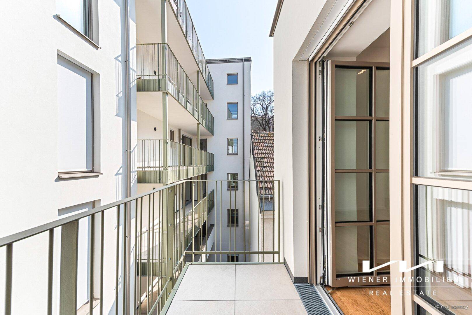 Schmaler Balkon mit Fliesenboden und Blick auf den Innenhof des modernen Wohnkomplexes.