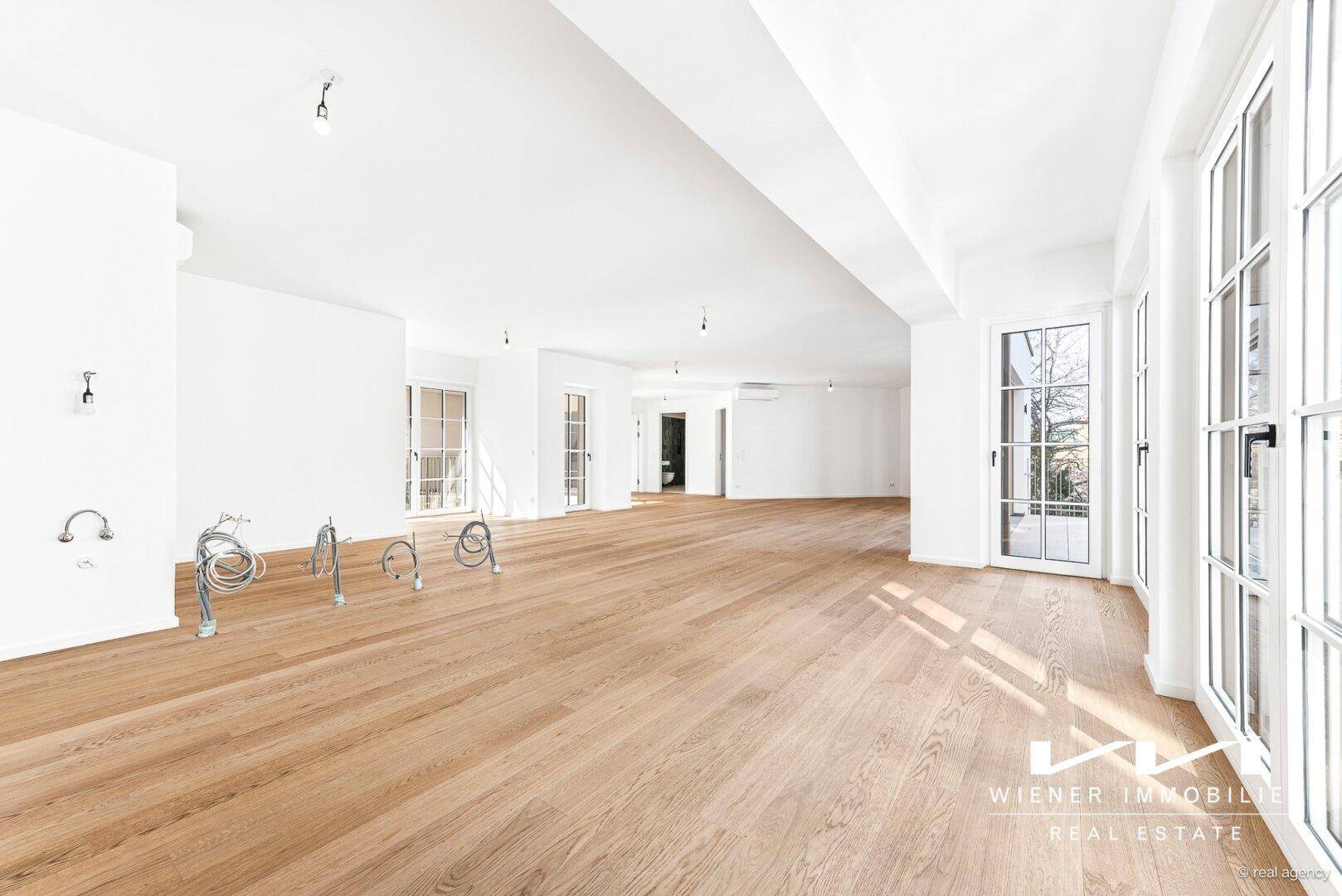 Geräumiger, heller Wohnbereich mit Eichenparkett und vorbereiteten Anschlüssen für eine offene Küche.