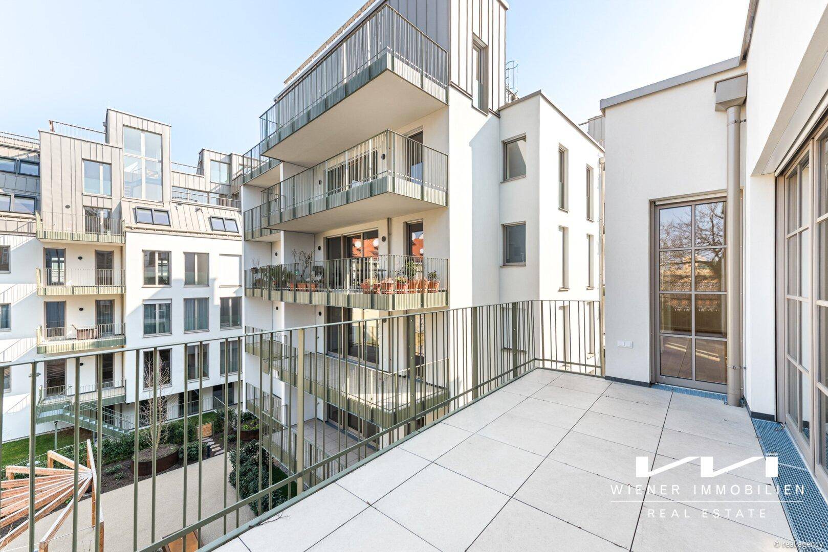 Geräumiger Balkon mit Fliesenboden und Blick auf den begrünten Innenhof des modernen Gebäudes. 