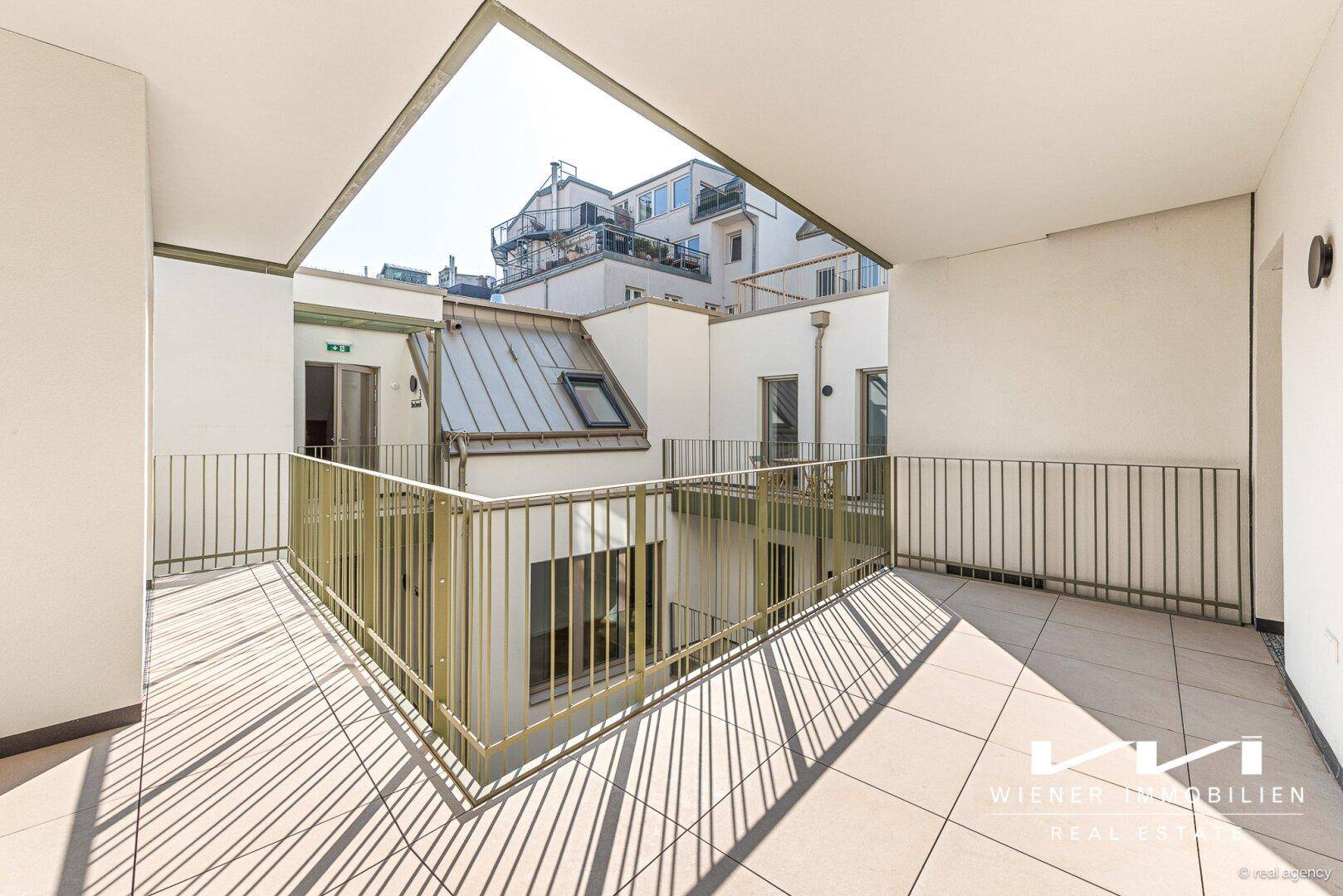 Große Dachterrasse mit Fliesenboden und sonnigem Blick auf die umliegenden Gebäude und den Innenhof.