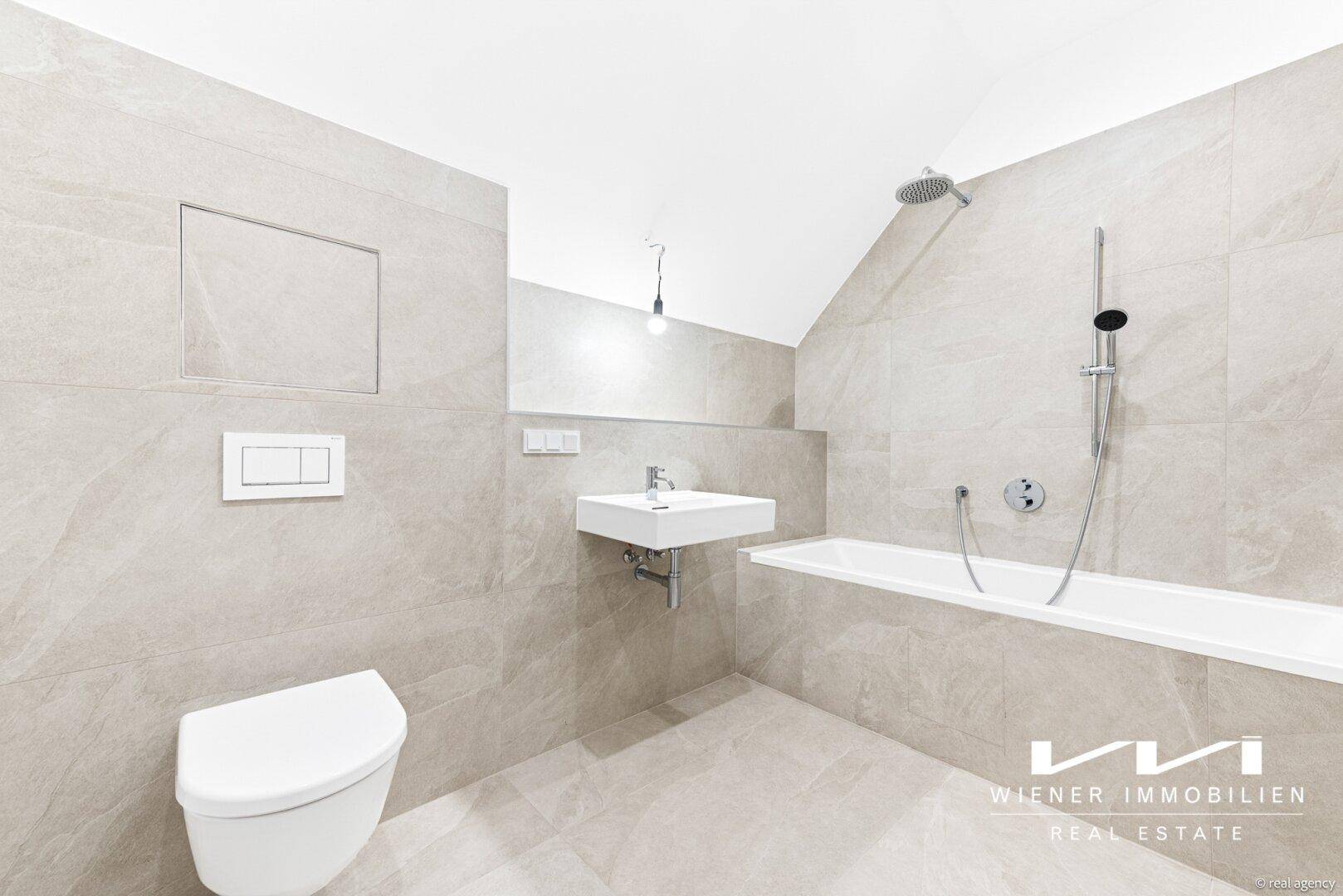 Modernes Badezimmer mit hellgrauen Fliesen, Badewanne und wandhängendem WC.