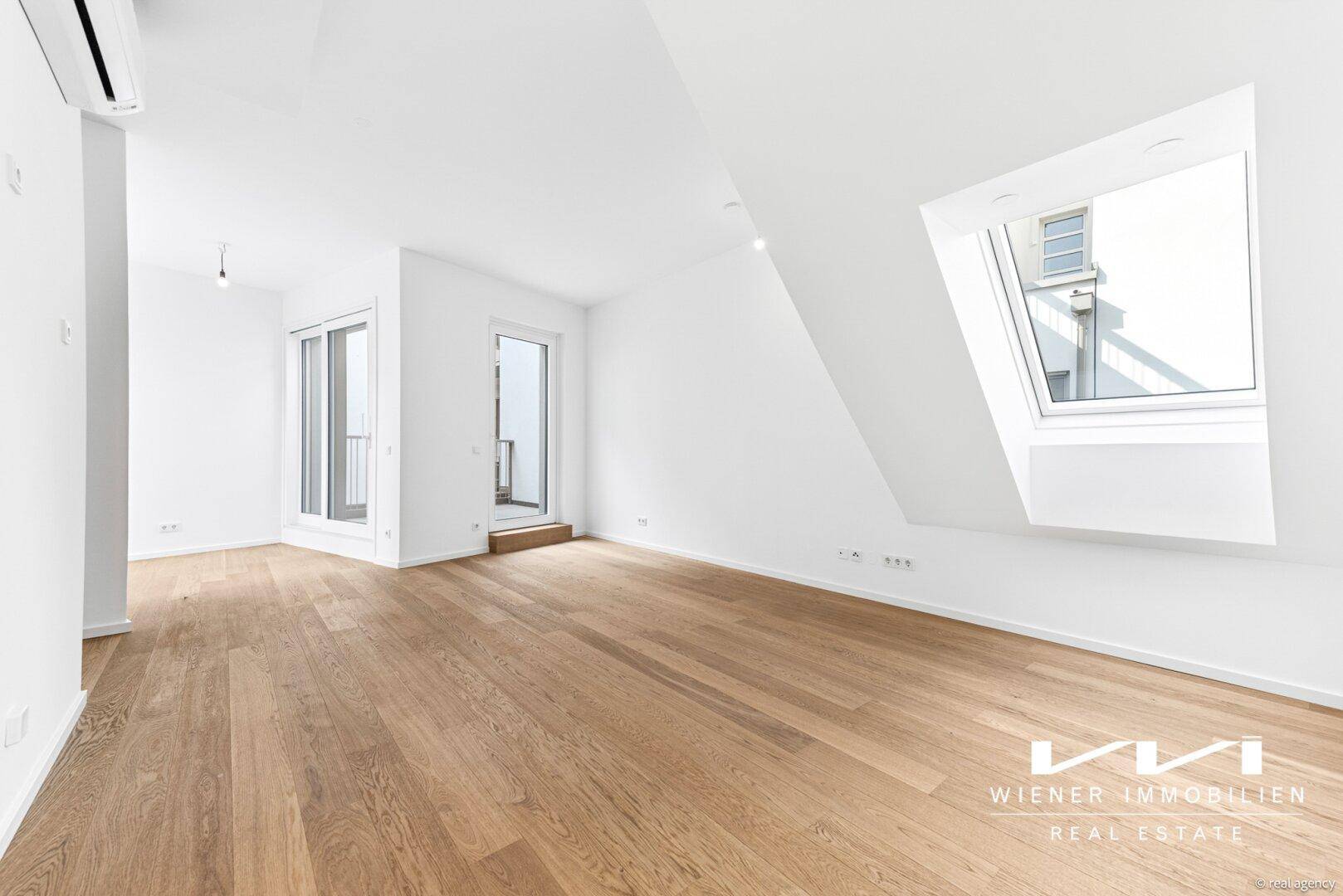 Lichtdurchfluteter Raum mit Holzboden, Dachfenster und Zugang zu einem Balkon.