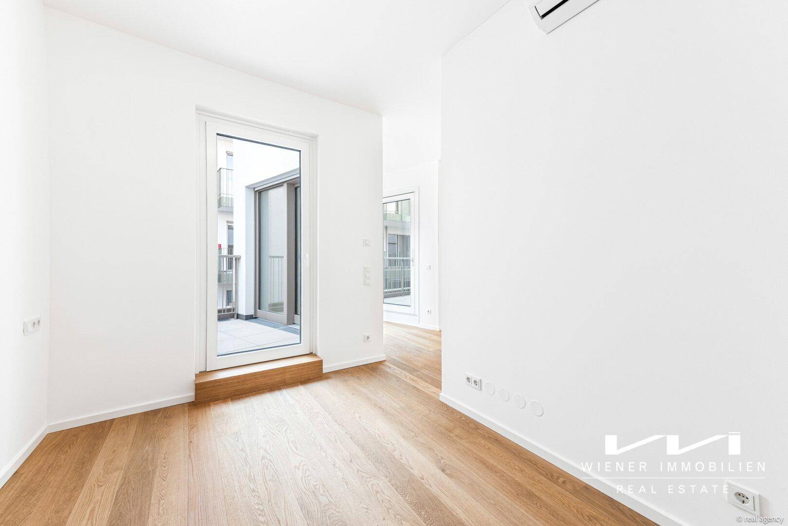 Moderner, heller Raum mit Holzboden und direktem Zugang zu einem Balkon.