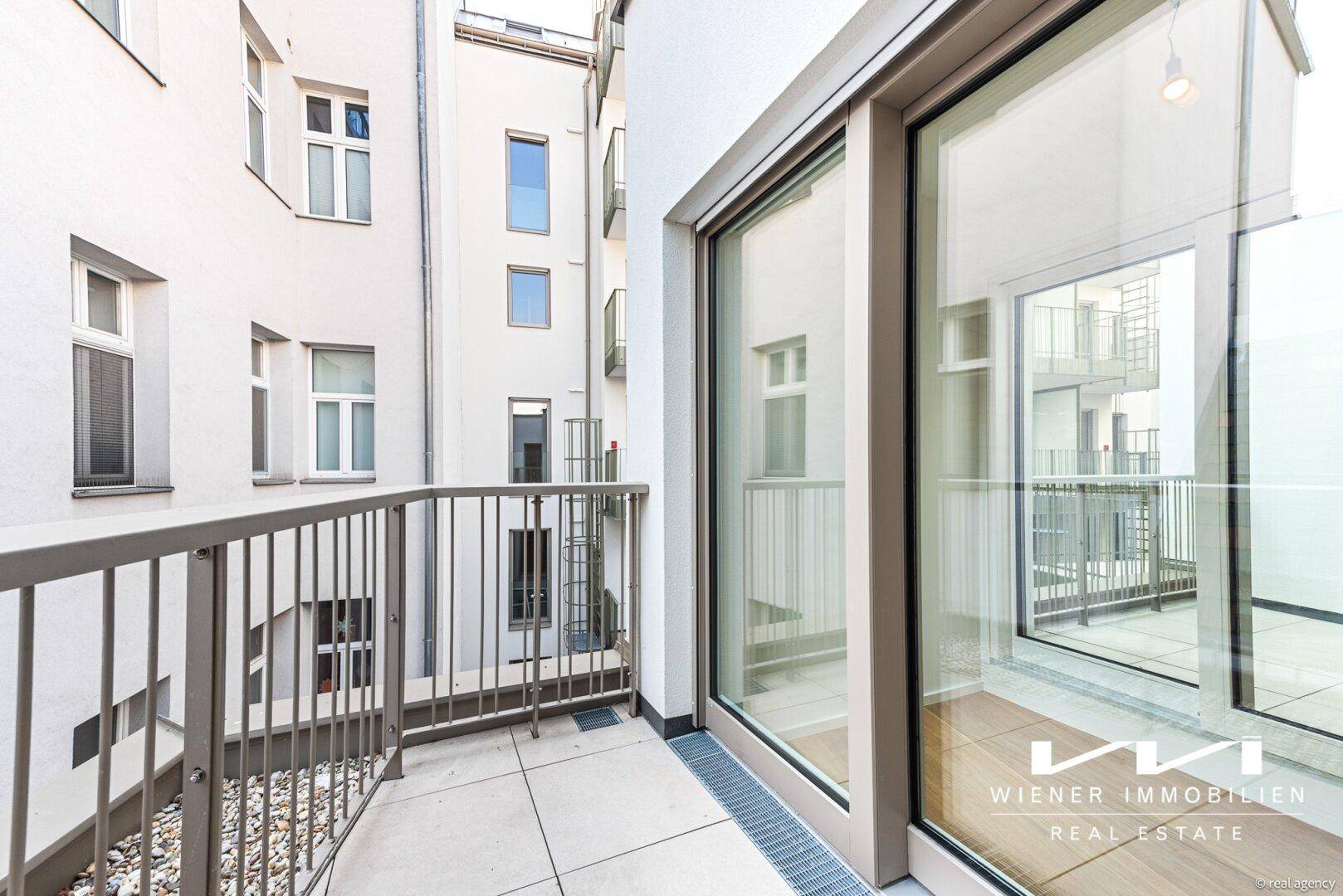 Kleiner Balkon mit Fliesenboden und Blick auf den ruhigen Innenhof des Gebäudes.