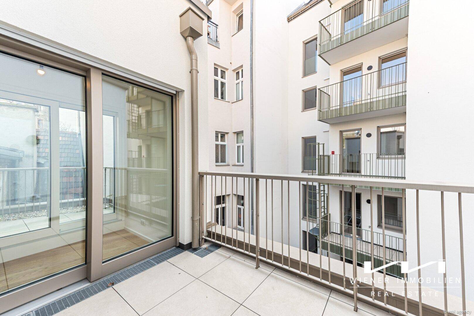 Kleiner Balkon mit Fliesenboden und Blick auf den Innenhof des Gebäudes.
