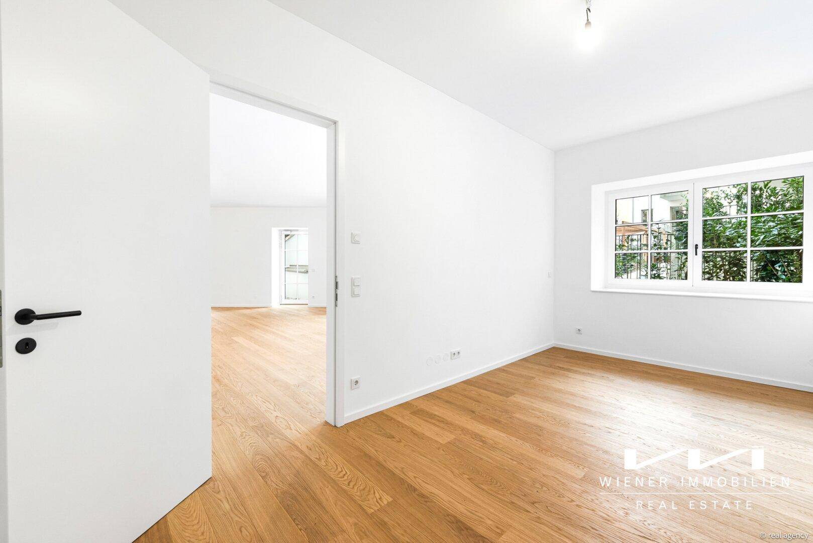 Helles Schlafzimmer mit Parkettboden und einem Fenster, das einen Blick ins Grüne bietet.