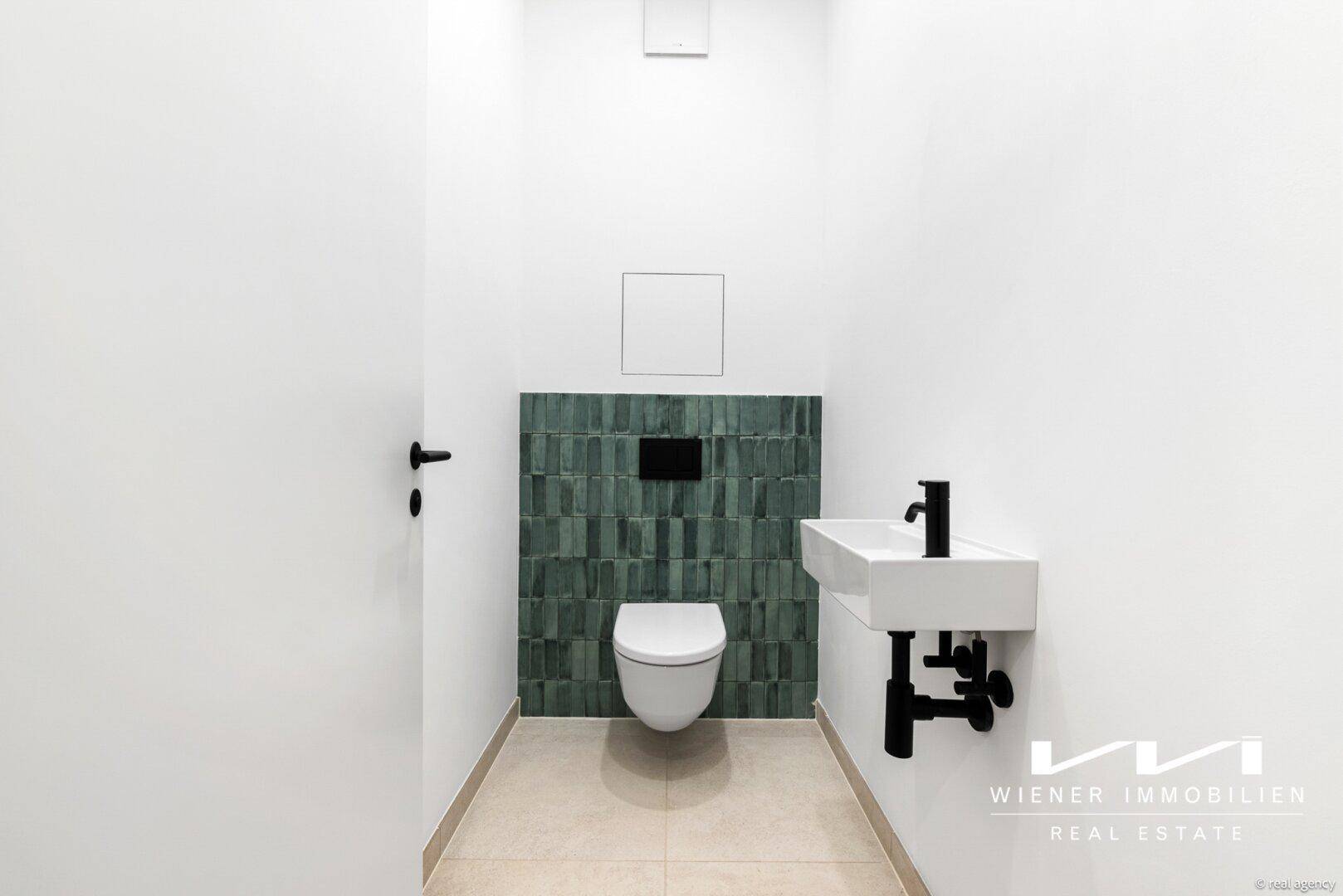 Modernes Gäste-WC mit grünen Akzentfliesen, Wand-WC und stilvollem Waschbecken.