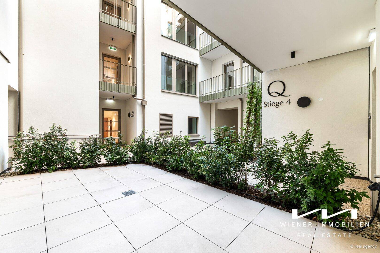 Moderner Innenhof eines Wohnkomplexes mit gepflegten Grünflächen und Zugang zu den Wohneinheiten.