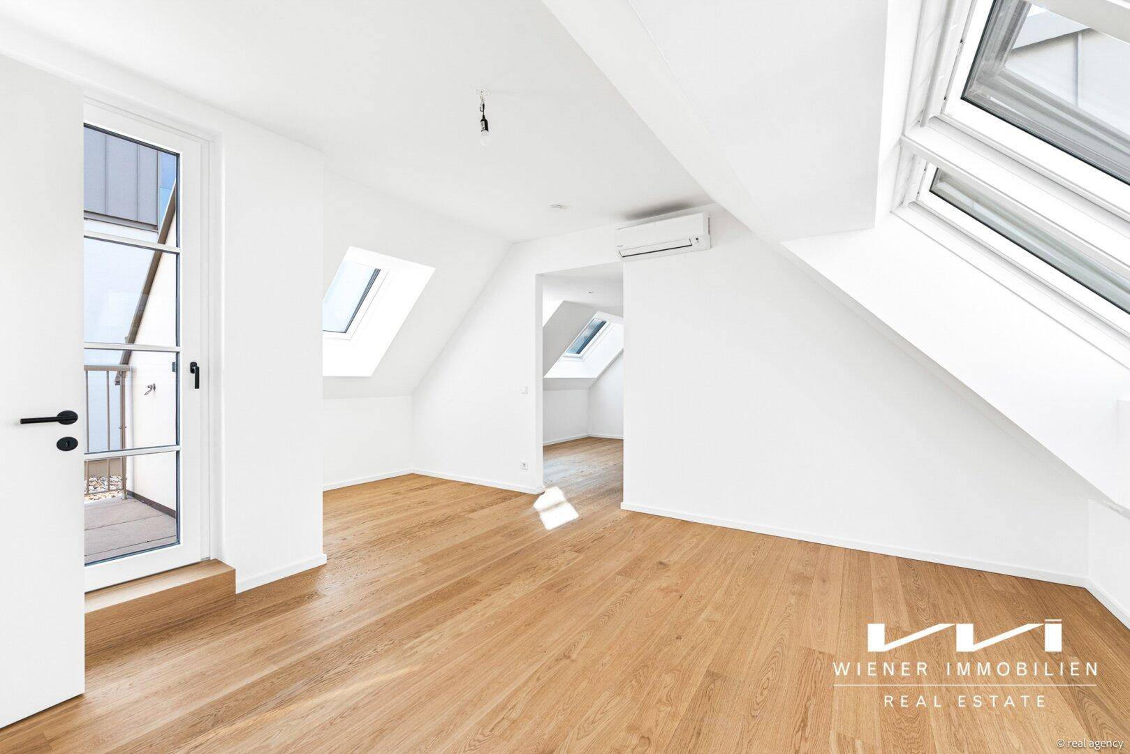Heller Wohnbereich im Dachgeschoss mit Holzparkett, Dachfenstern und Zugang zu einem französischen Balkon.