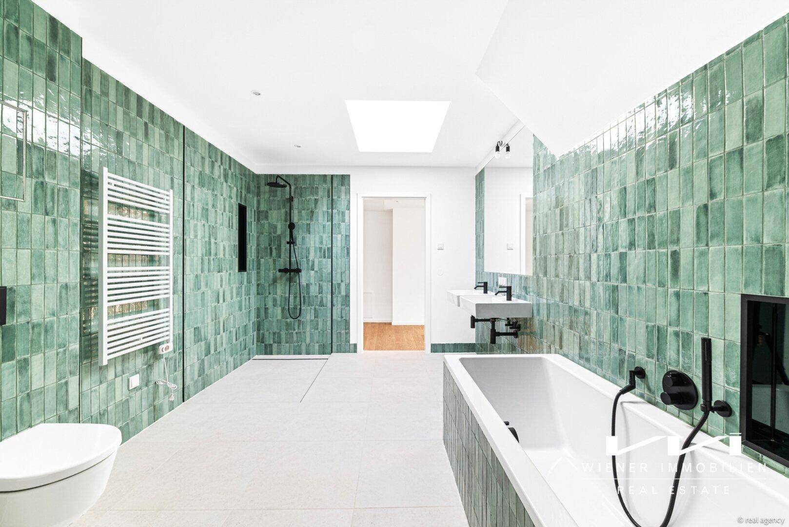 Modernes Badezimmer mit grünen Fliesen, Badewanne, Dusche und Doppelwaschbecken unter einem Oberlicht.