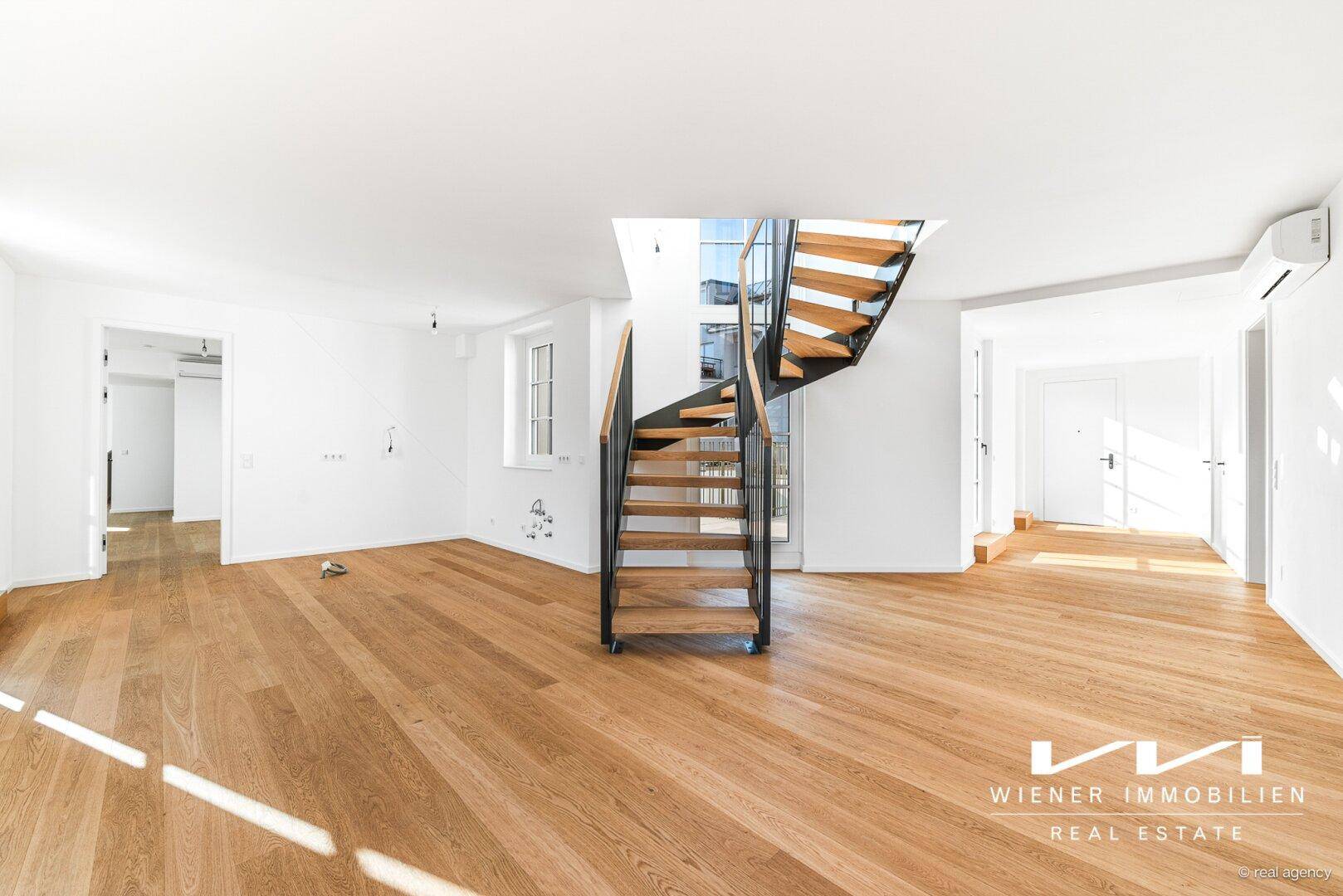 Offener, heller Wohnbereich mit Holzparkettboden, großen Fenstern und einer modernen Wendeltreppe.