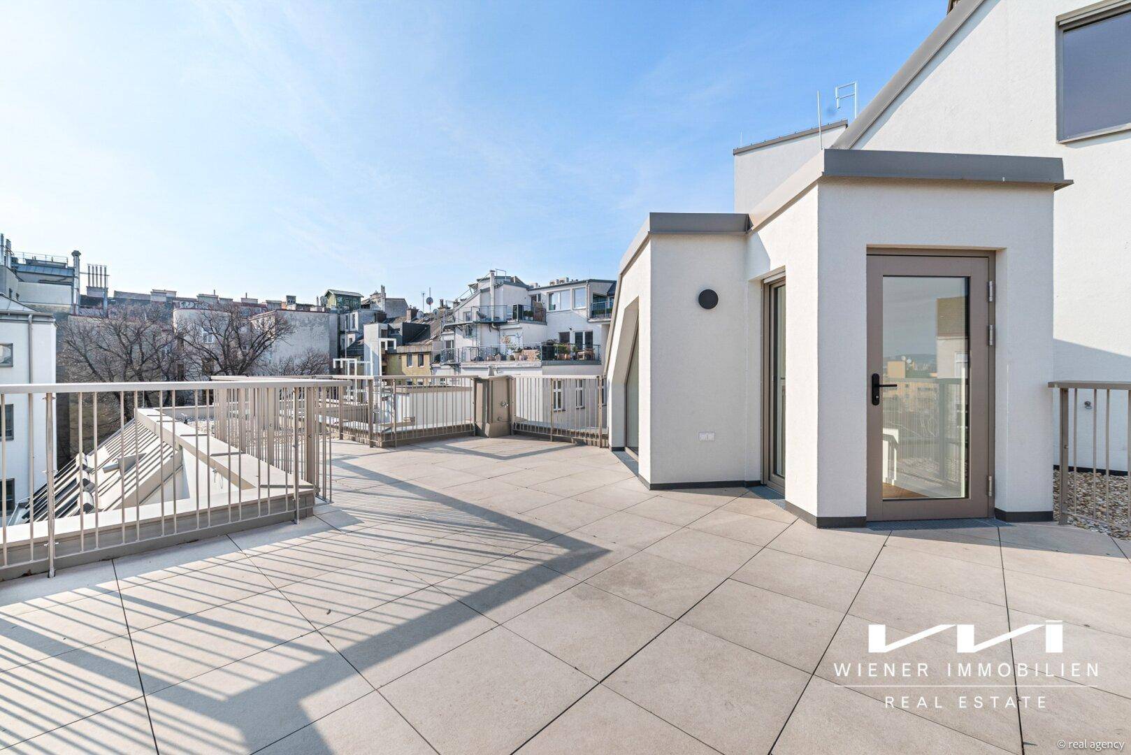 Geräumige Dachterrasse mit Fliesenboden und Blick auf die umliegenden Gebäude der Stadt.