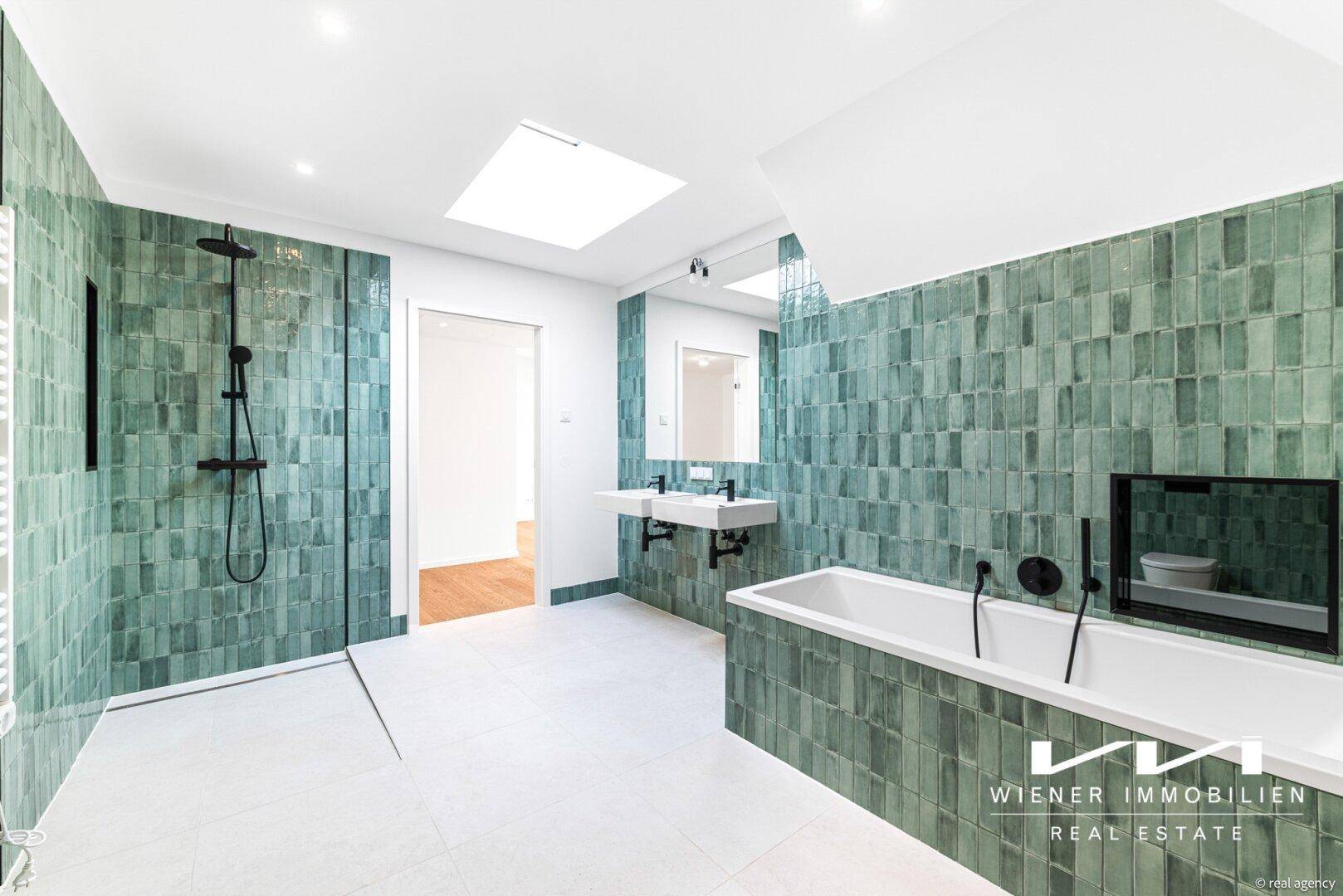Modernes Badezimmer mit grünen Fliesen, Badewanne, Dusche und Doppelwaschbecken unter einem Oberlicht.