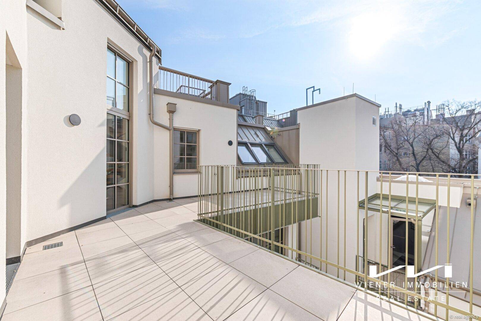 Weitläufige Dachterrasse mit Fliesenboden und Blick auf die umliegenden Dächer und Gebäude.