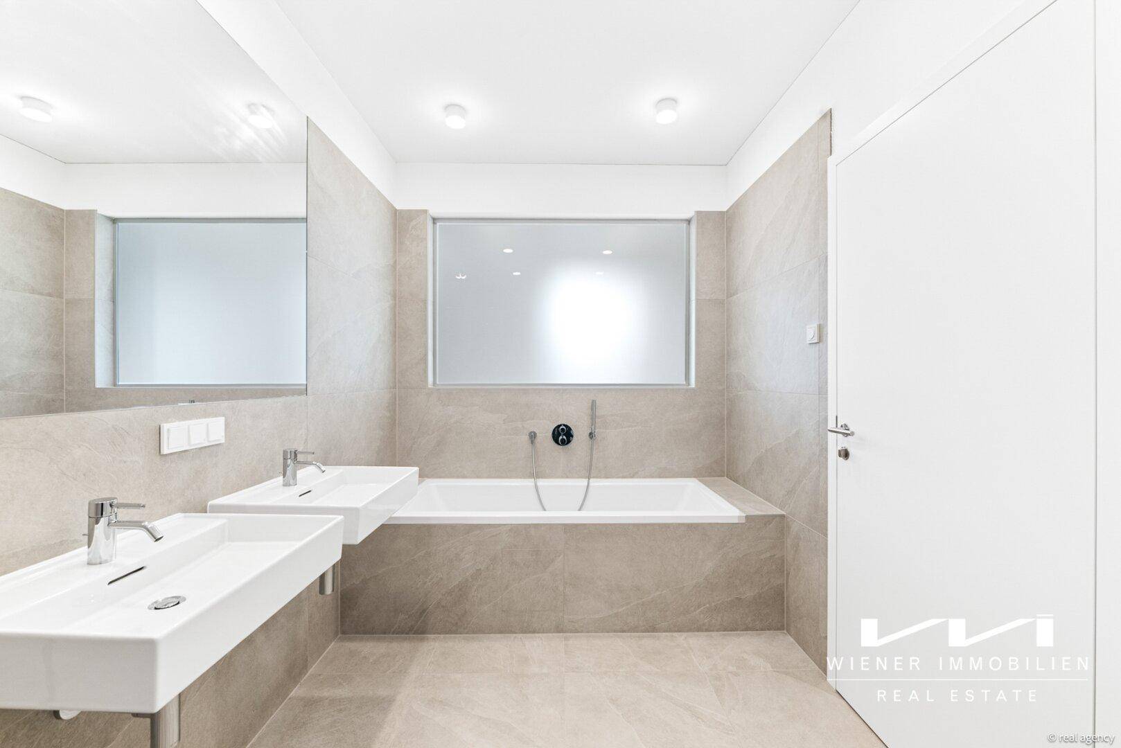 Modernes Badezimmer mit Doppelwaschbecken, Badewanne und großen hellen Fliesen an Wänden und Boden.